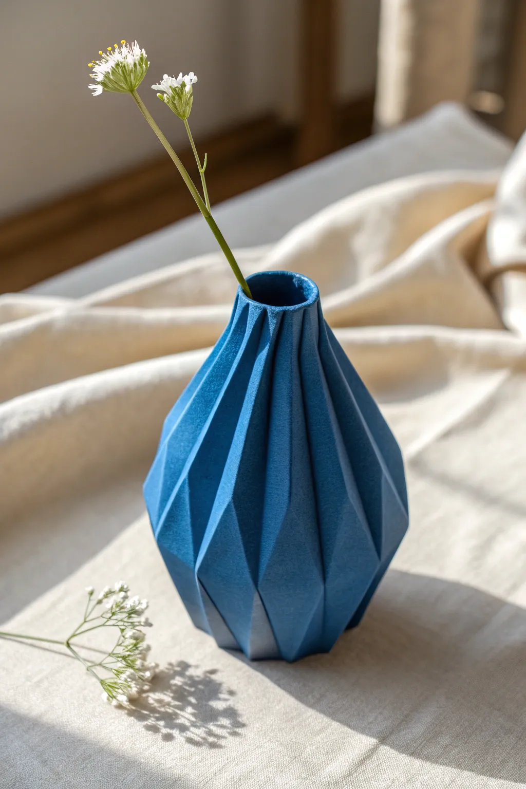 Folded soft-slab paper vase in bold matte cobalt, letting the creases and silhouette shine