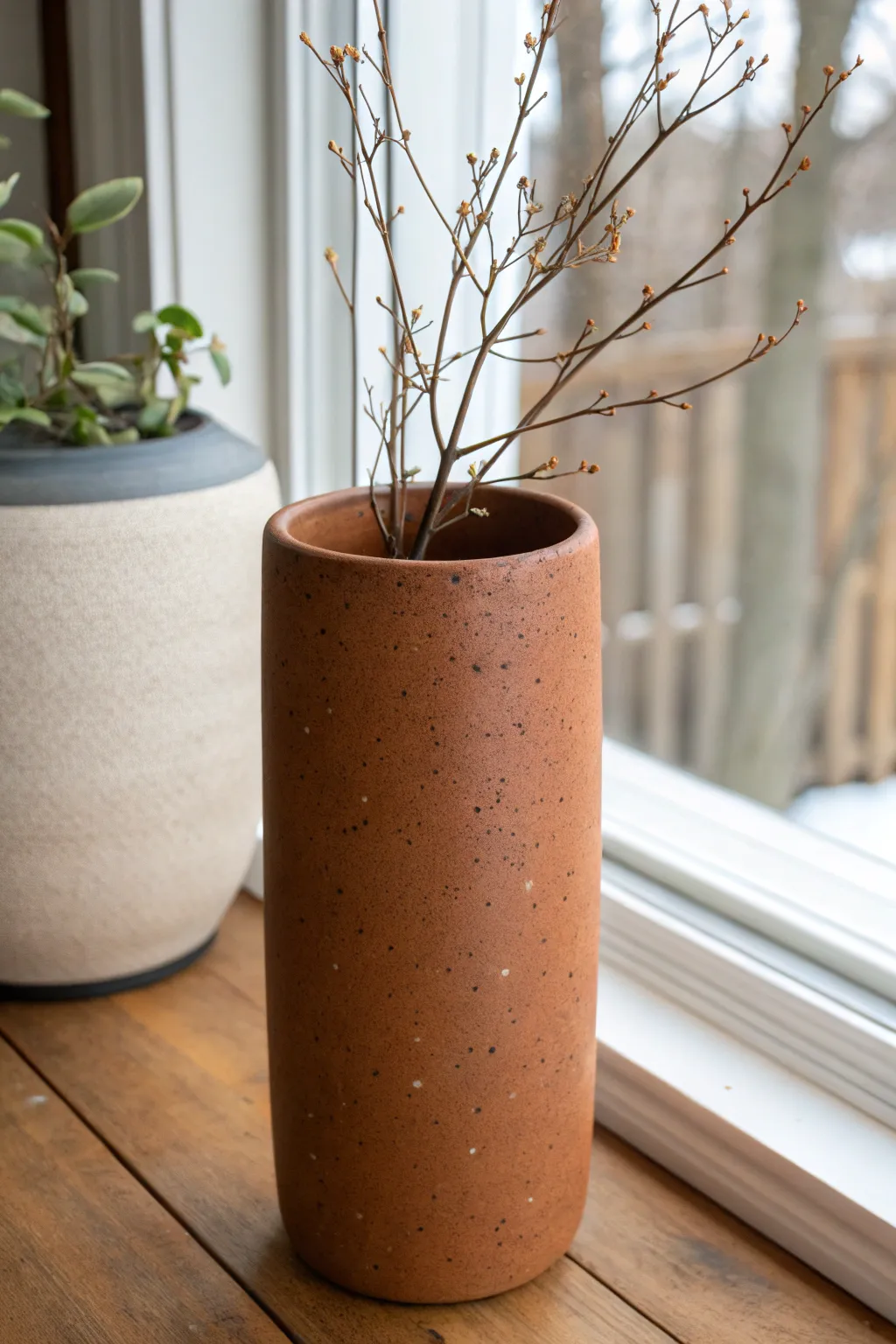 Oval slab cylinder vase with a single branch, minimalist form and bold earthy color contrast.