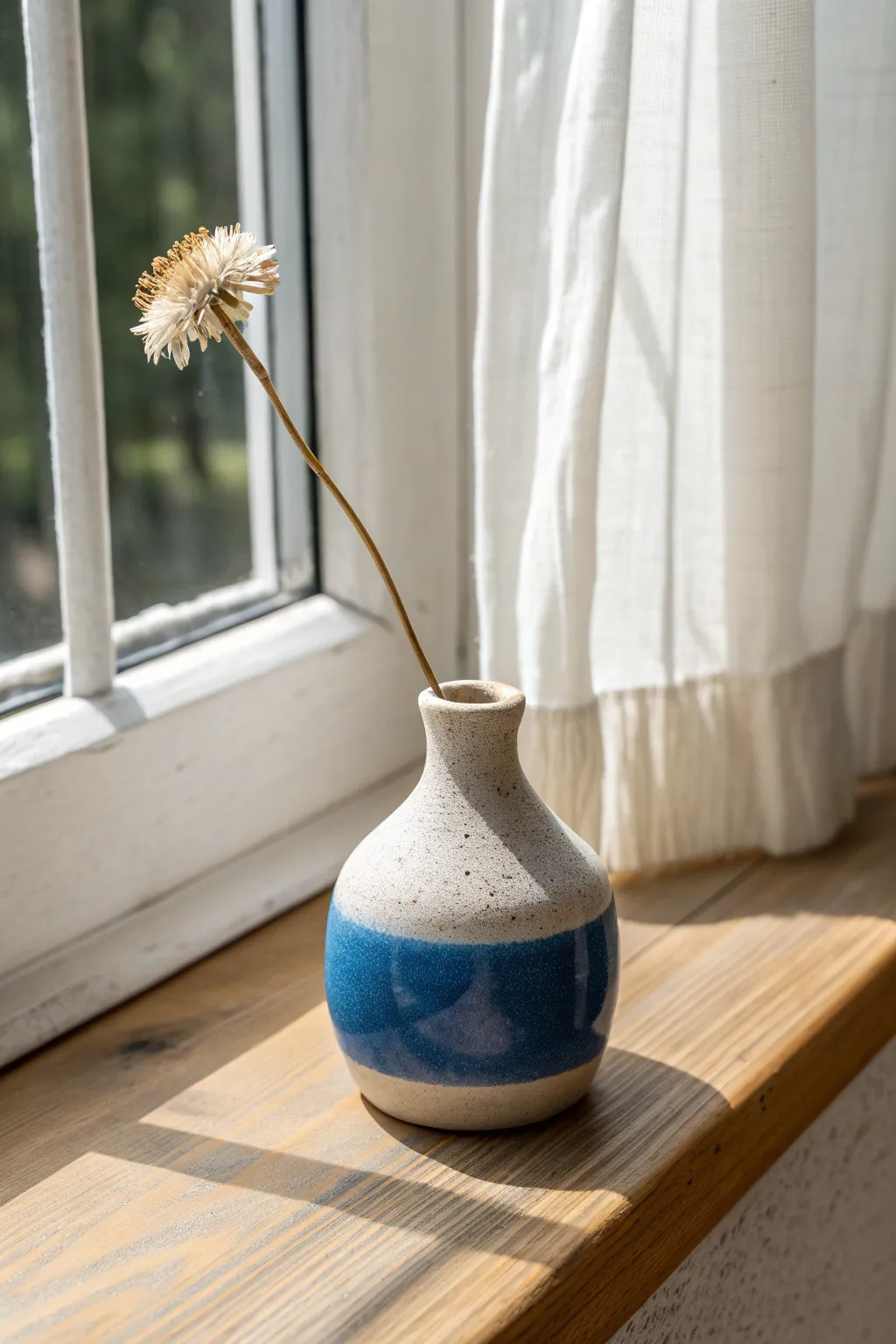 Tiny handmade bud vase on a sunlit sill, minimalist Scandinavian style with a bold pop of color