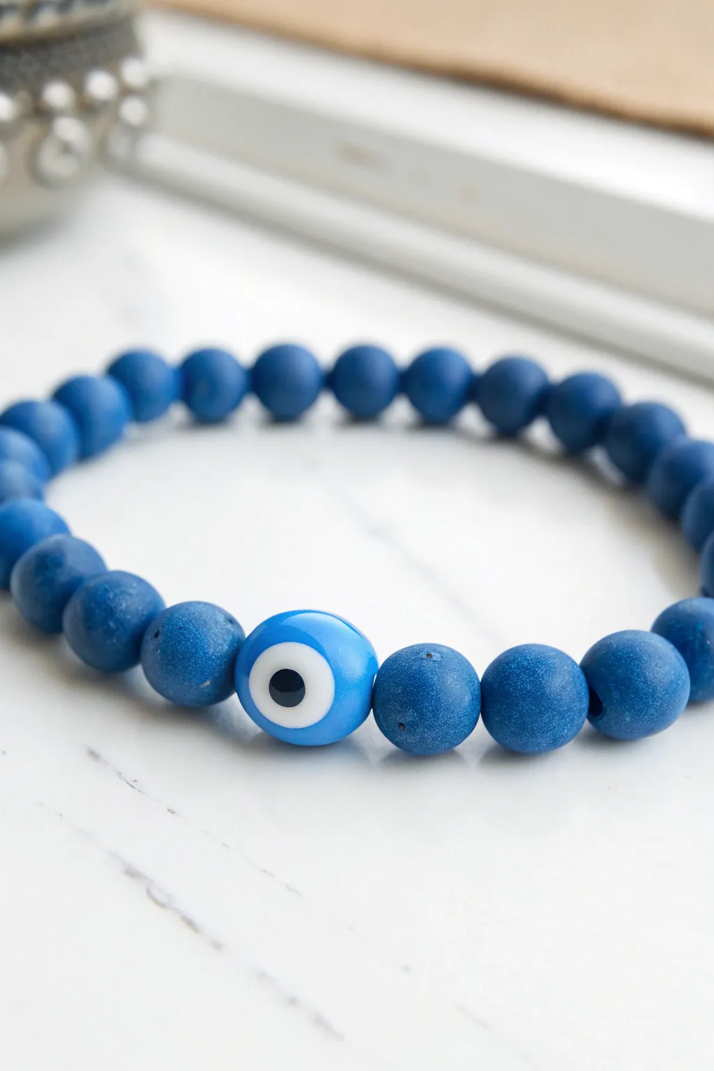 Minimal blue clay bead bracelet with a blue-and-white protective eye focal on clean white.