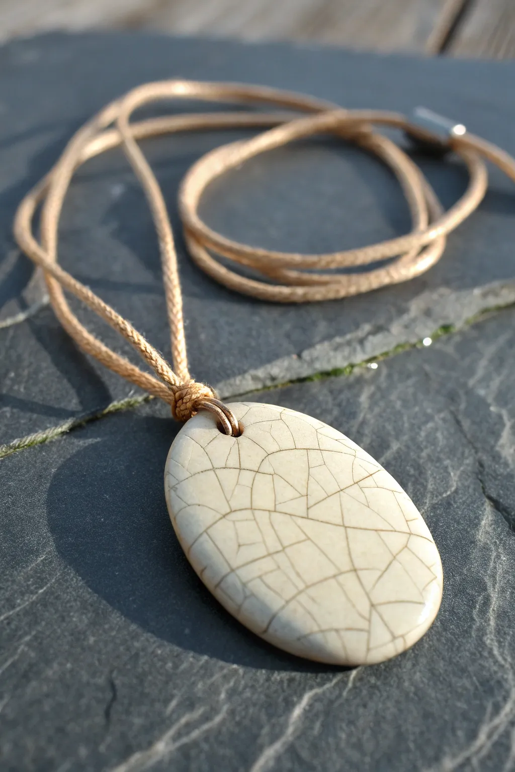 Ivory crackle-glaze ceramic pendant on dark slate, minimalist and handcrafted texture focus