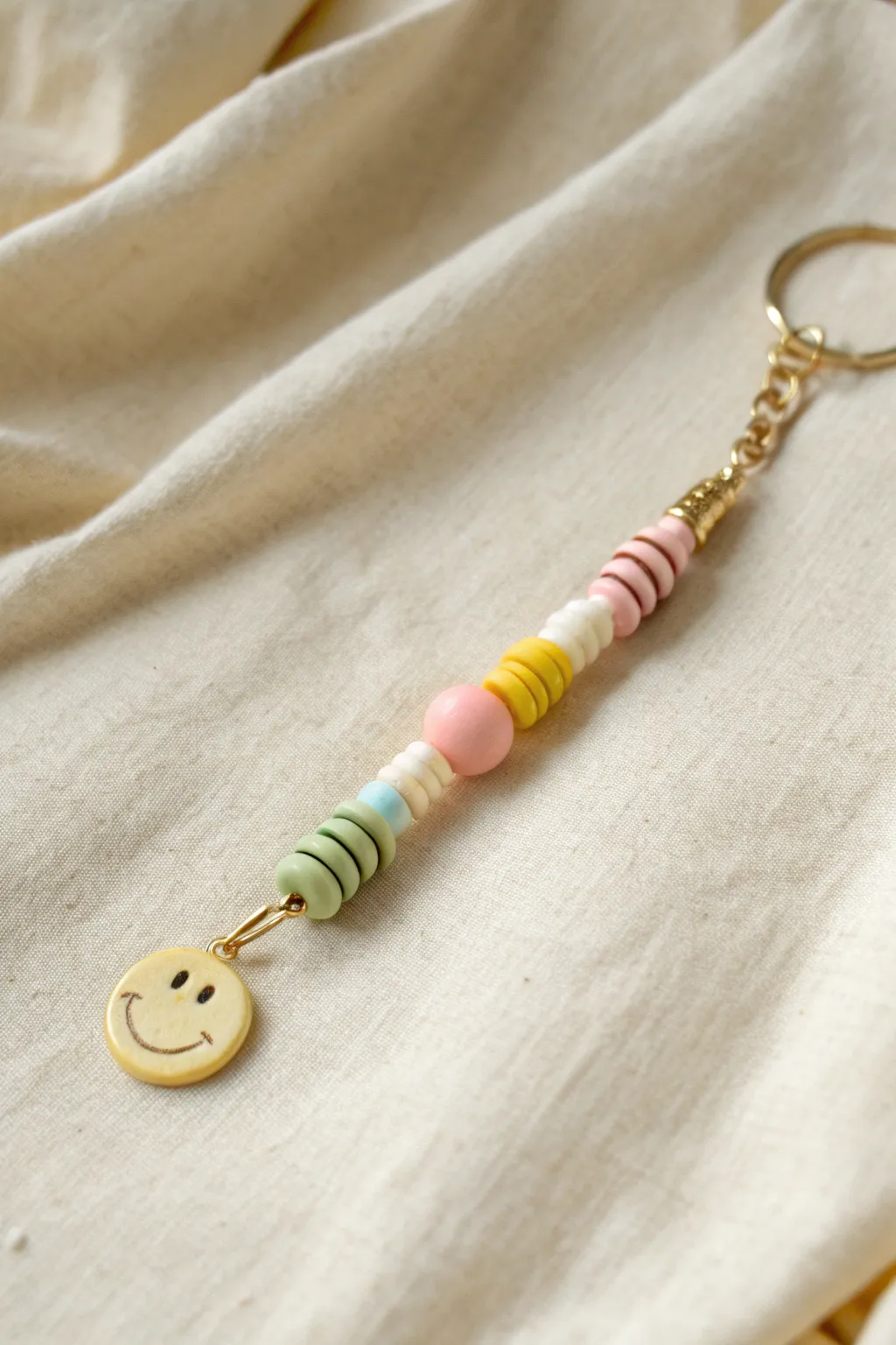 Pastel heishi bead keychain with a centered smiley bead, minimal and cheerful with soft contrast.
