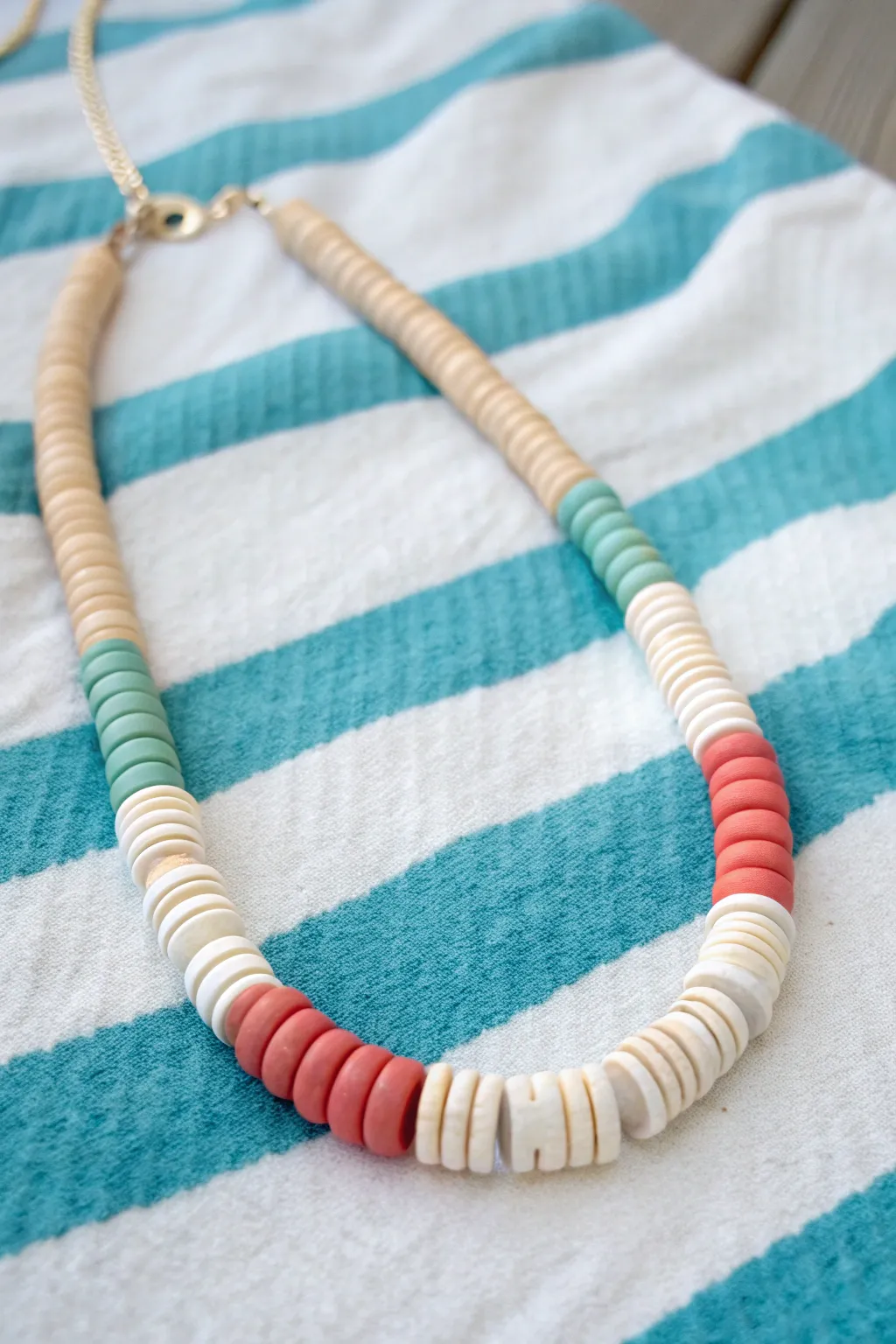 Chunky spacer heishi surf necklace in summer tones, styled on a striped towel for beachy minimal vibes.