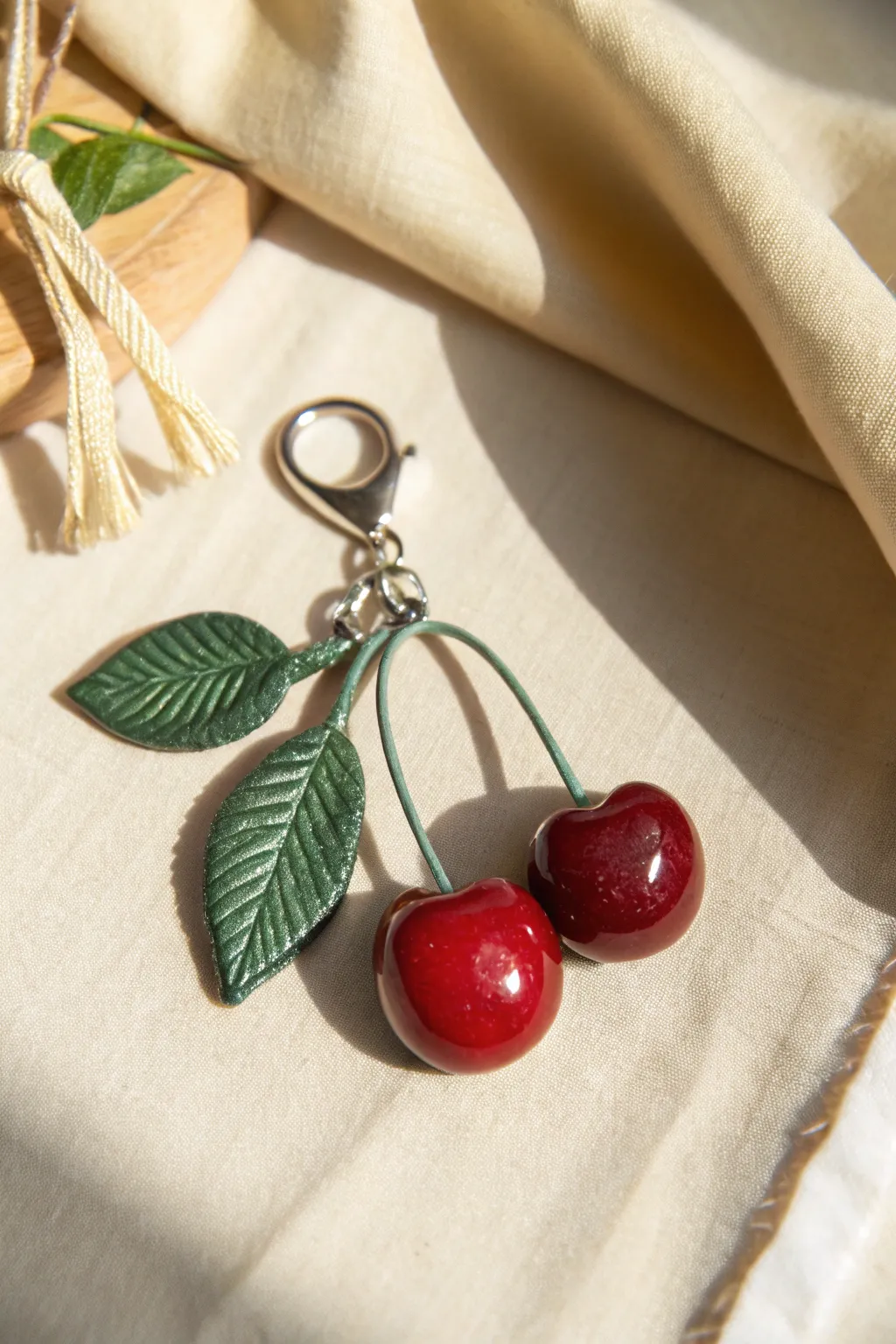 Deep red cherry pair charm with curved stems and a tiny leaf, simple, glossy, and handmade.