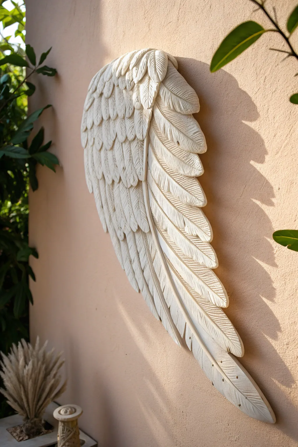 Matte clay feather wing plaque with layered quills, hung on a pale wall with soft shadow depth.