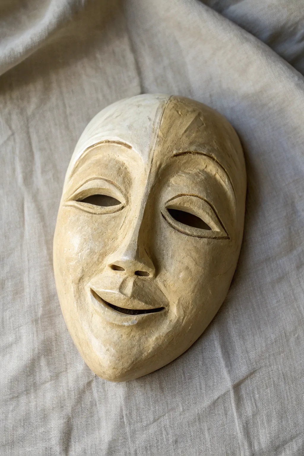 A split clay mask with a smile and frown, using warm and cool glazes for bold contrast