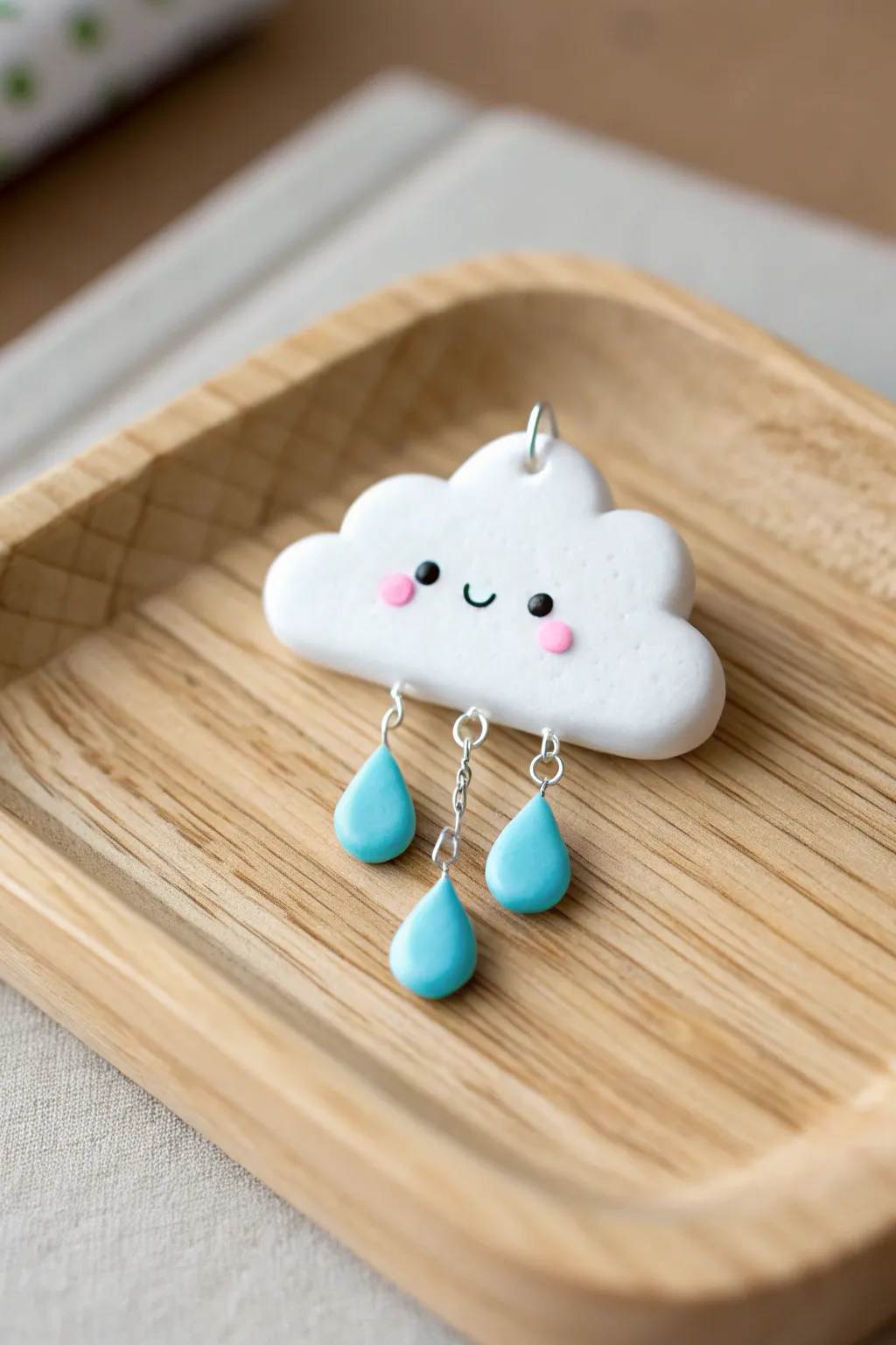 Tiny rain cloud charm with sweet face and dangling raindrops in soft blue and white.