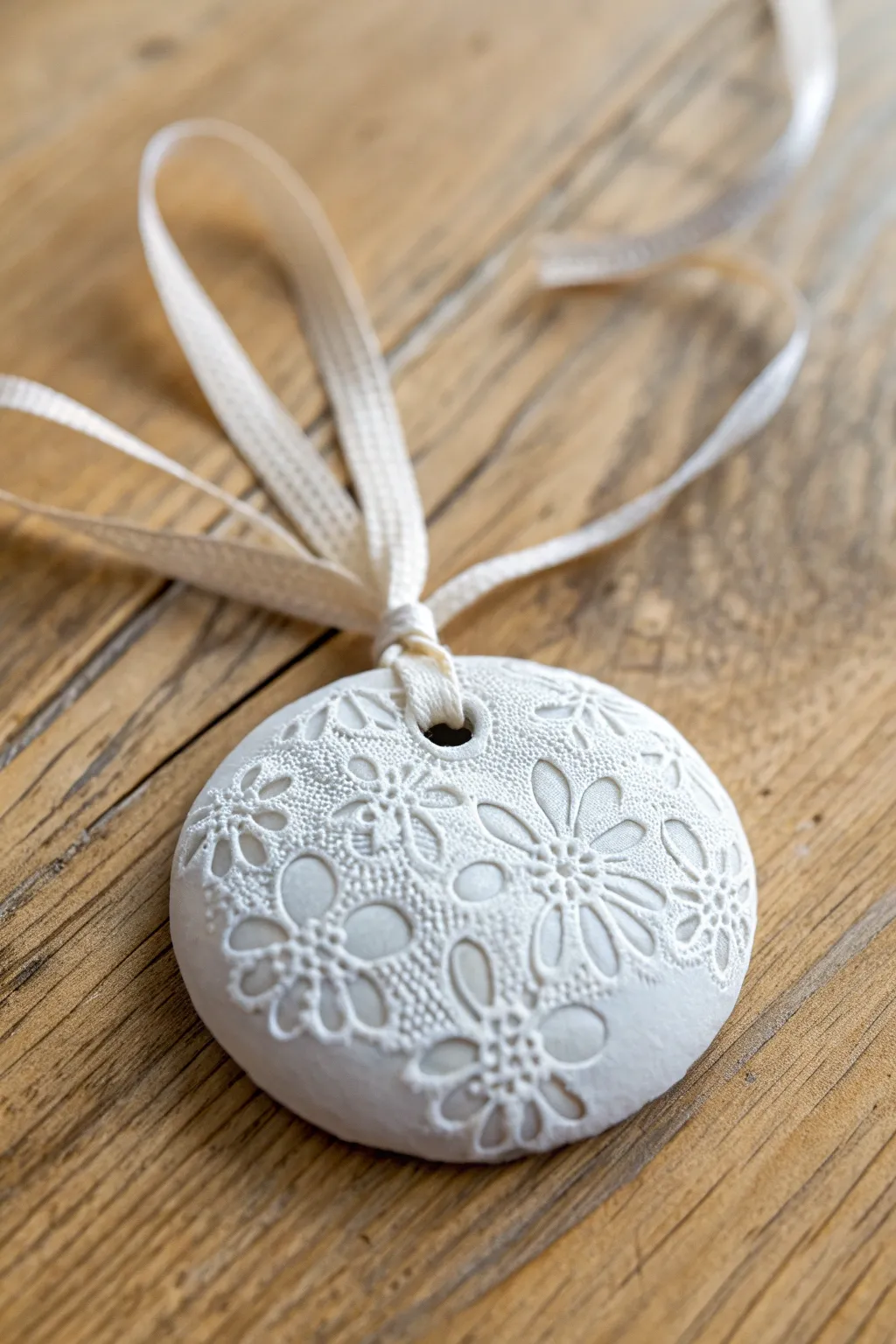 Lace-pressed snowy clay ornament with soft shadows and a ribbon, simple and festive.