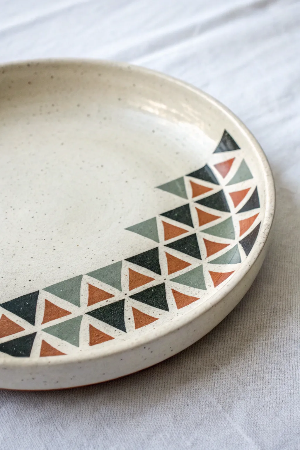 Minimalist ceramic plate with a corner cluster of stencil-like triangles in earthy tones