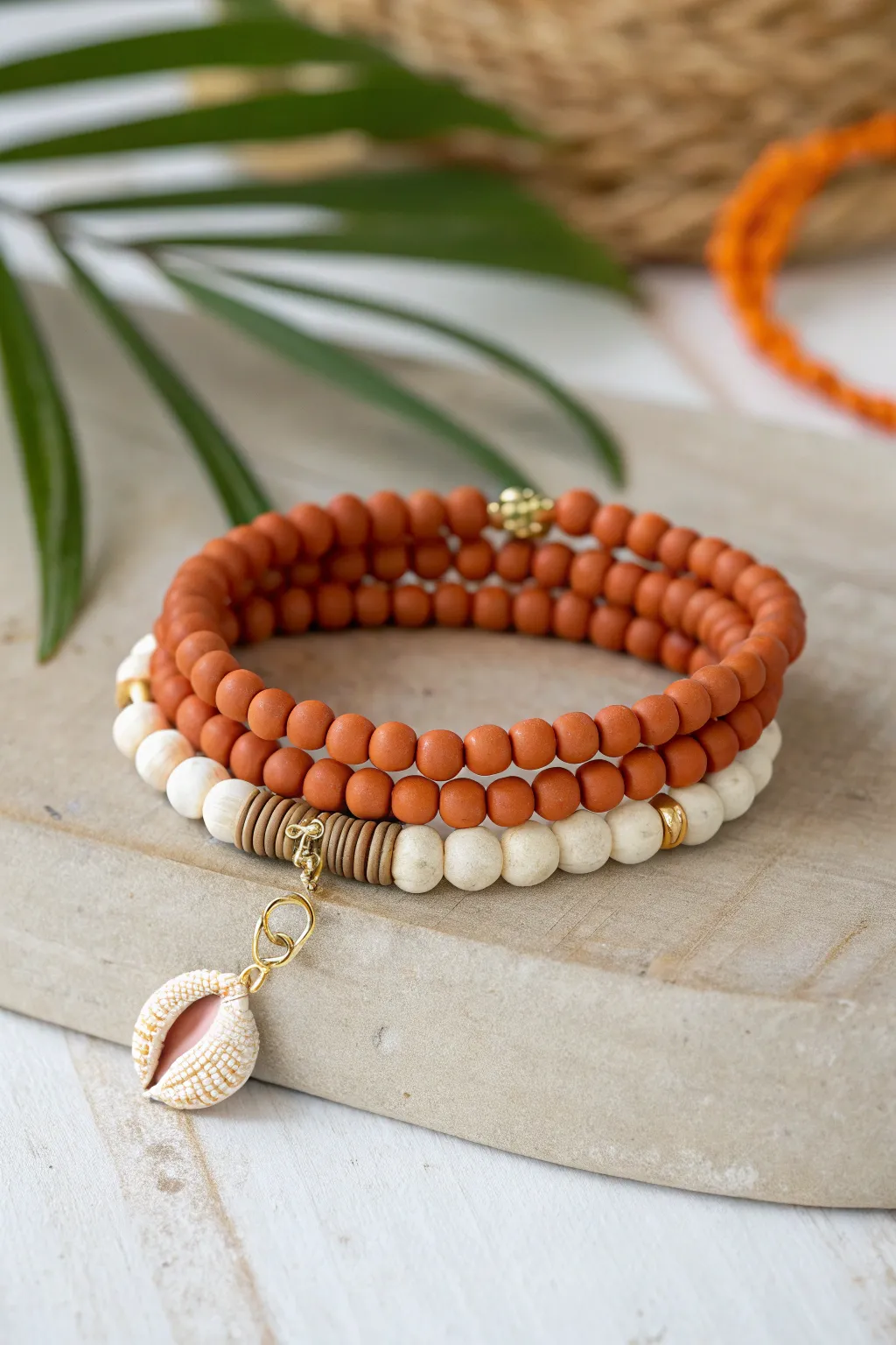 Sun-kissed orange clay bead stack with tiny shell charm, paired with soft neutral bracelets.
