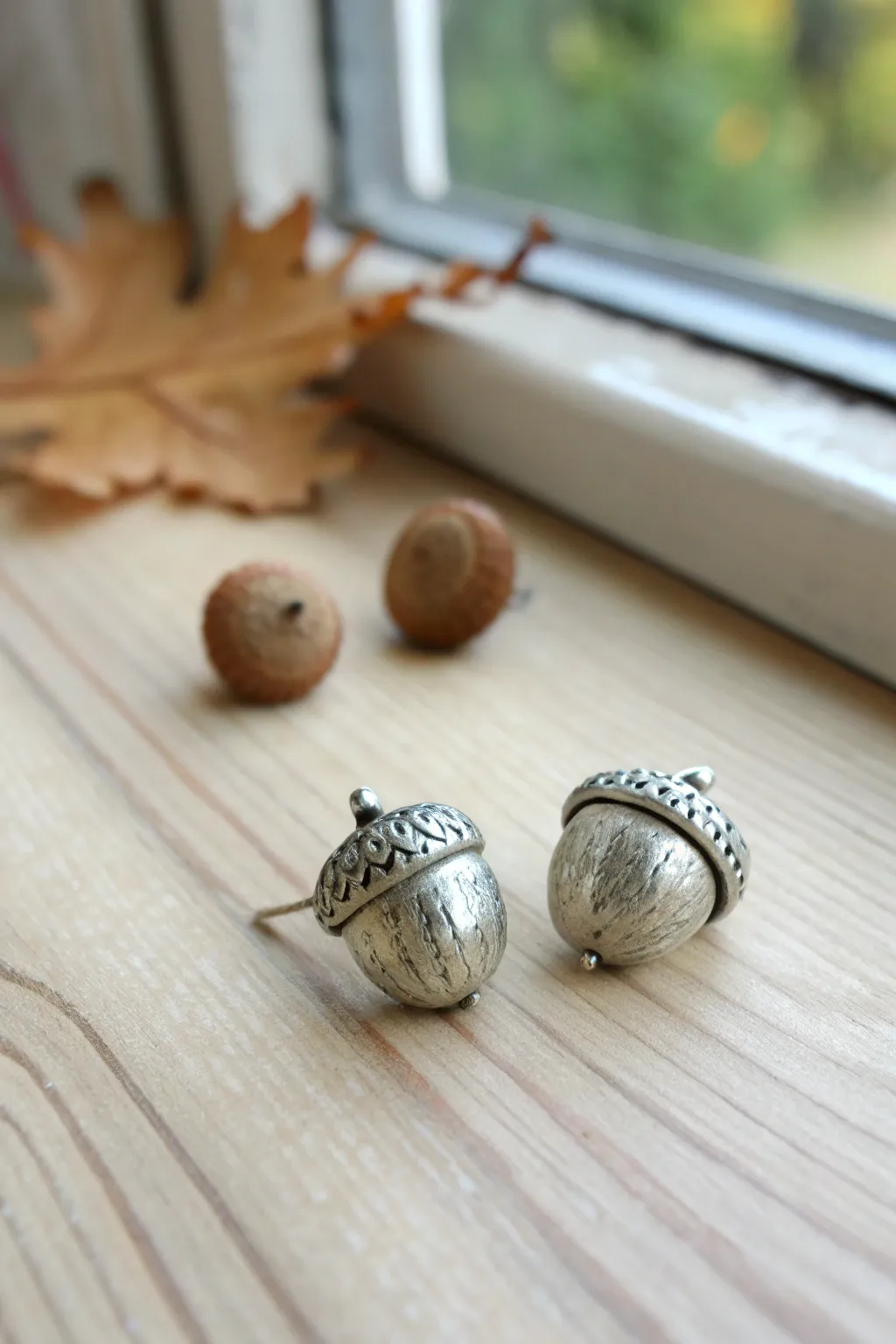 Minimal silver acorn cap button studs with soft patina, styled simply on pale wood.
