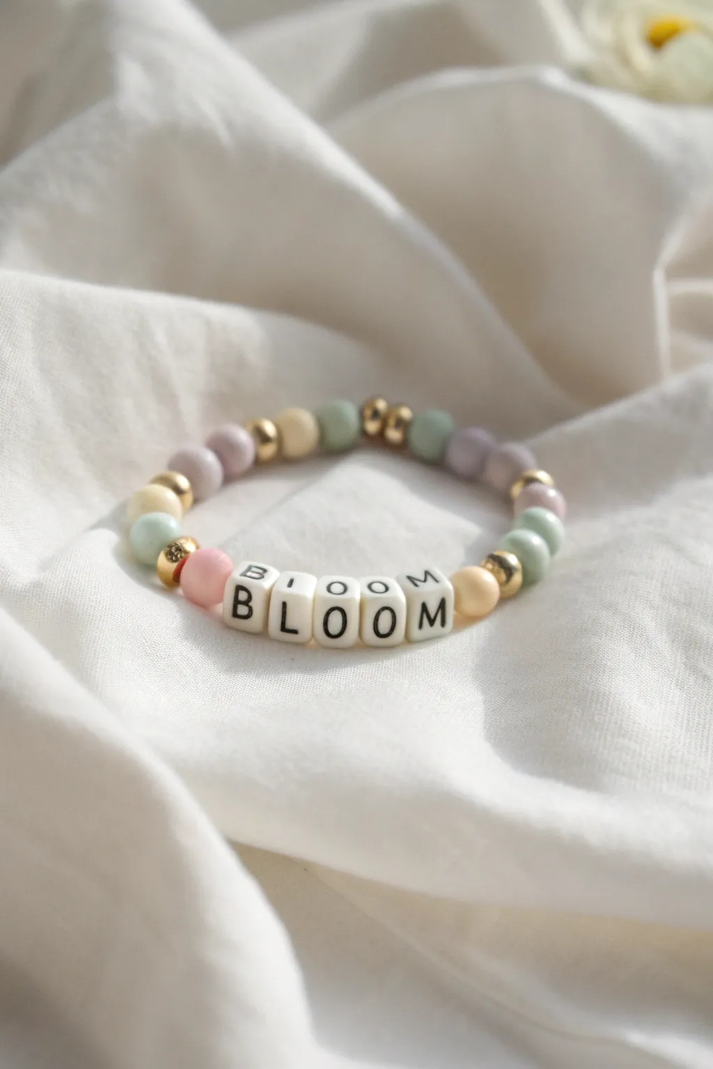 Spring clay bead bracelet with BLOOM centerpiece, pastel discs and gold spacers on white linen.