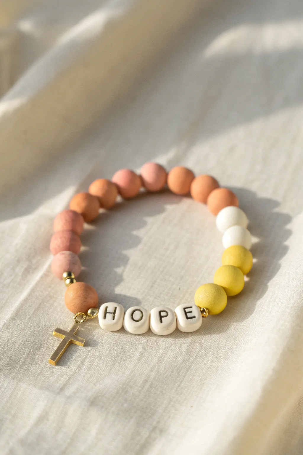 Sunrise clay bead bracelet in peach and coral with a tiny cross charm, a gentle reminder of hope.