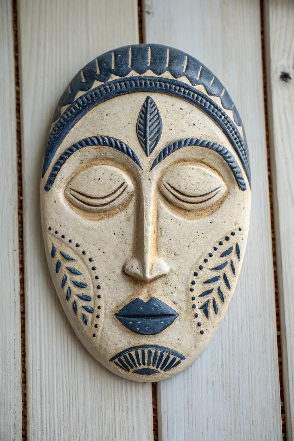 Bold ceramic face wall plaque in matte ivory with dark recessed texture, ideal for high school.