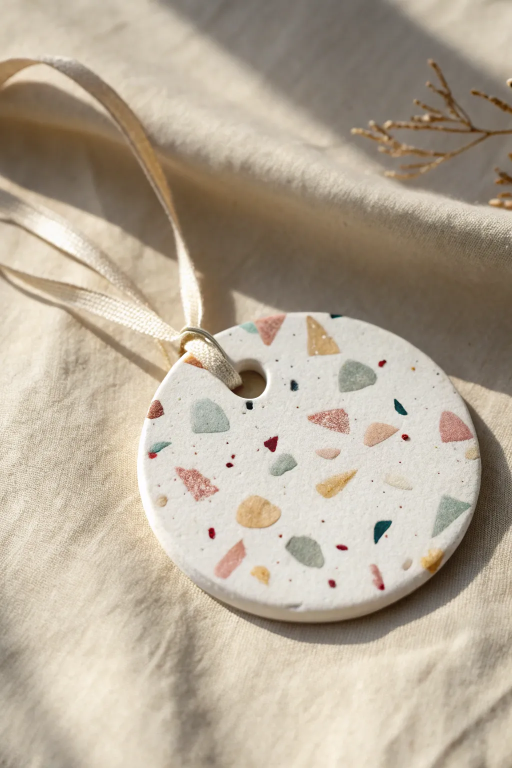 Minimalist terrazzo clay ornament with confetti speckles and linen ribbon, modern festive charm.
