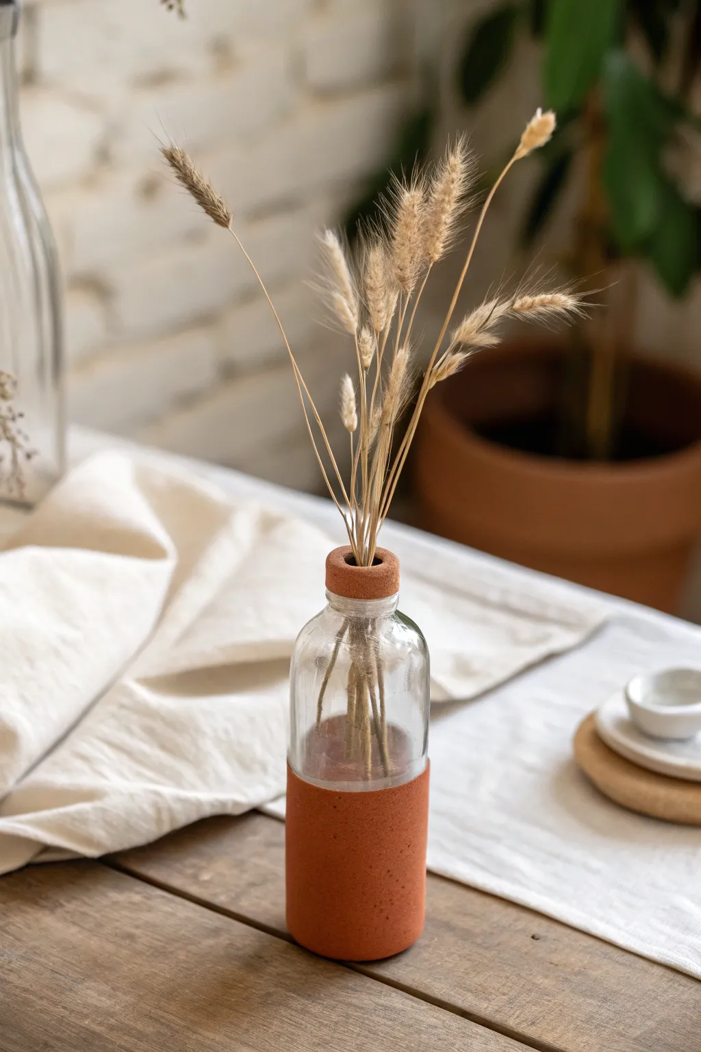 Minimal terracotta sleeve vase over glass, styled with linen and a few airy stems.