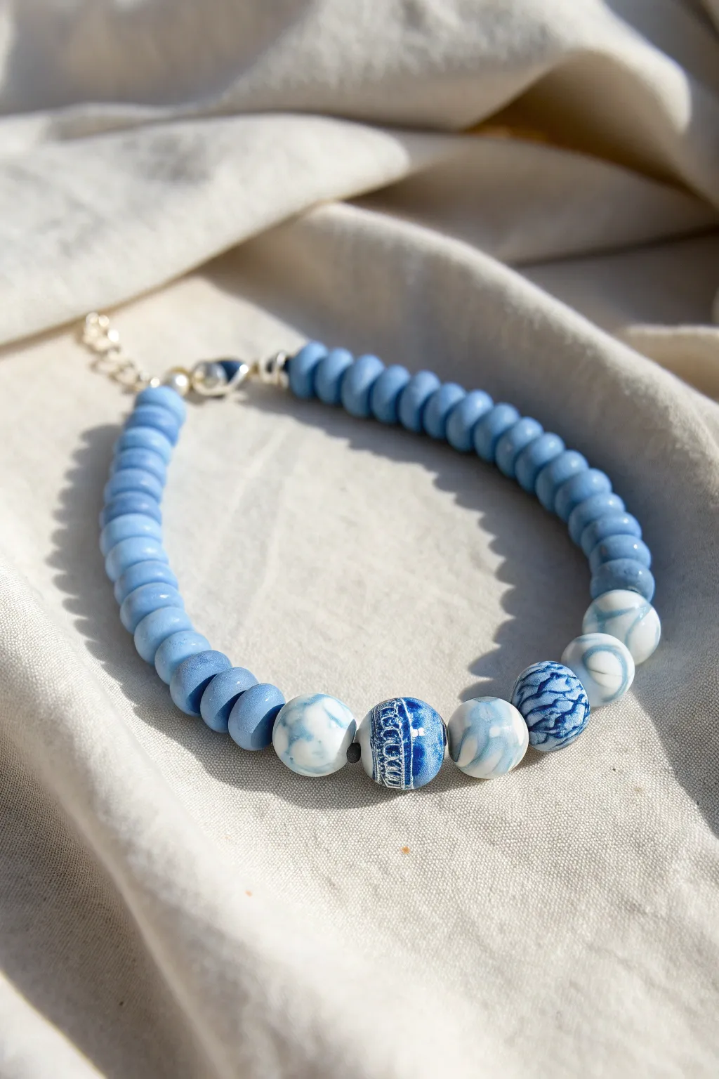 Minimalist blue heishi bracelet with bold blue-and-white marble swirl statement beads on linen.