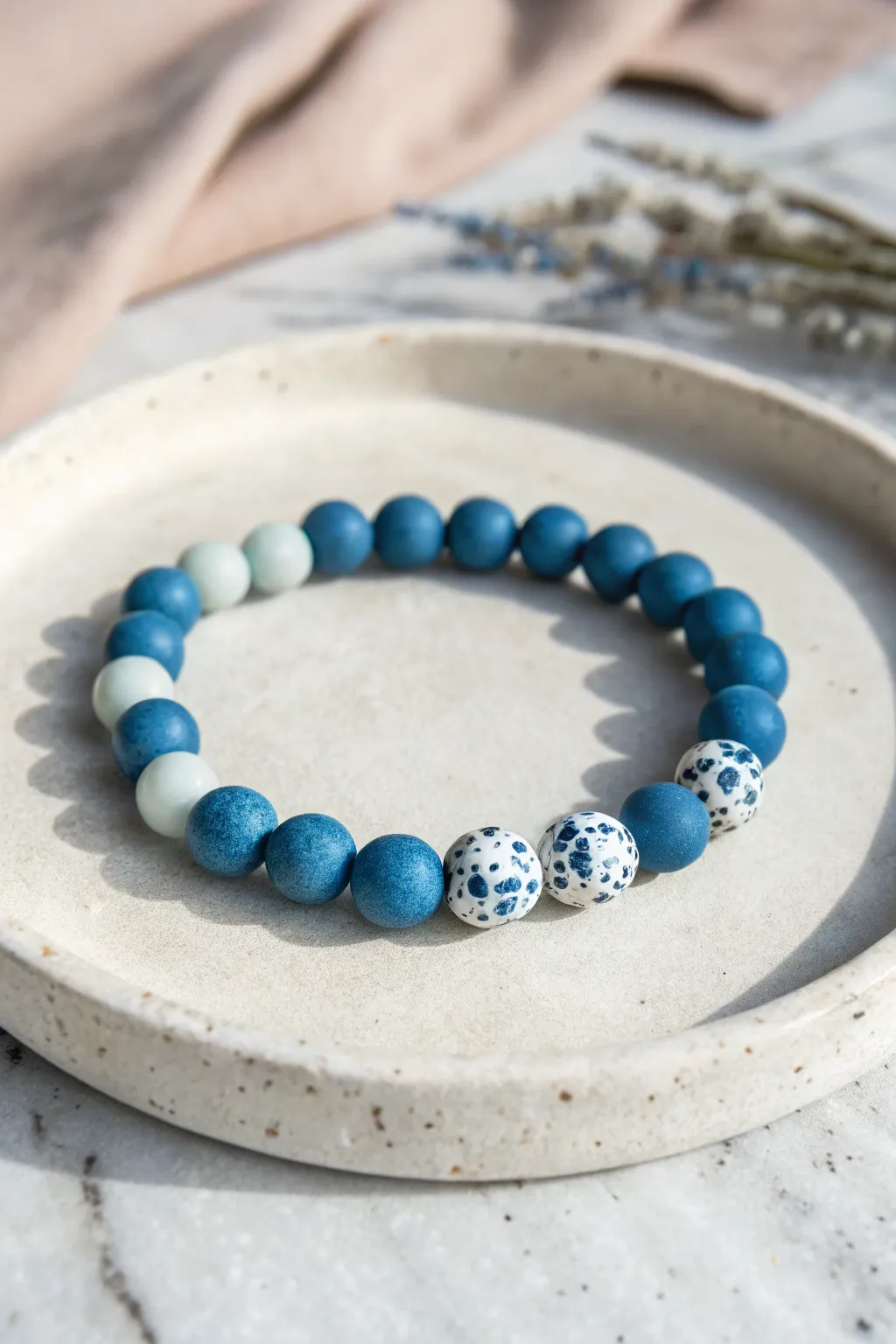 Blue clay bead bracelet with terrazzo speckles on a clean stone backdrop, modern and serene.