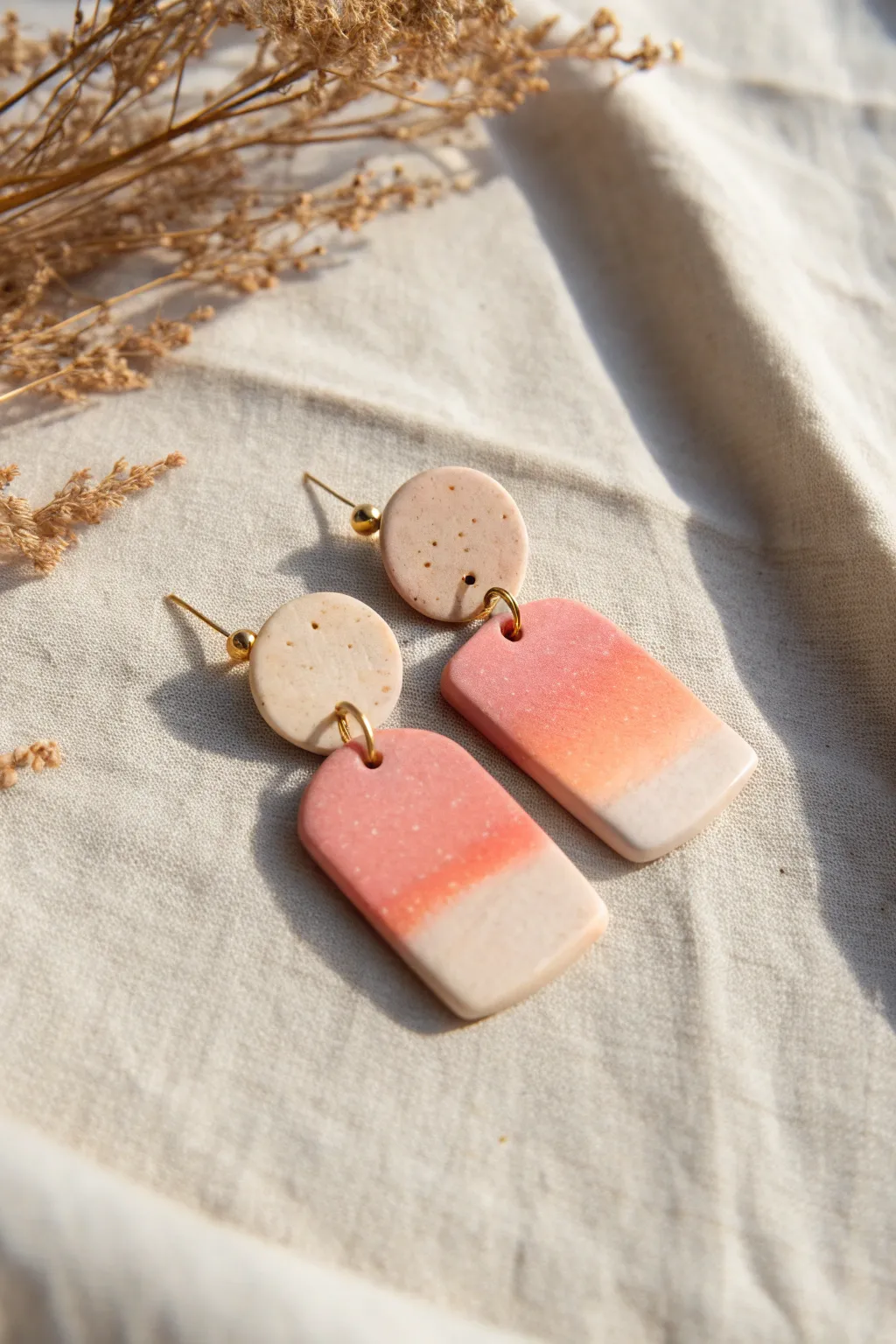 Soft blush-to-peach ombre tab earrings in a clean Scandinavian flat lay with boho warmth.