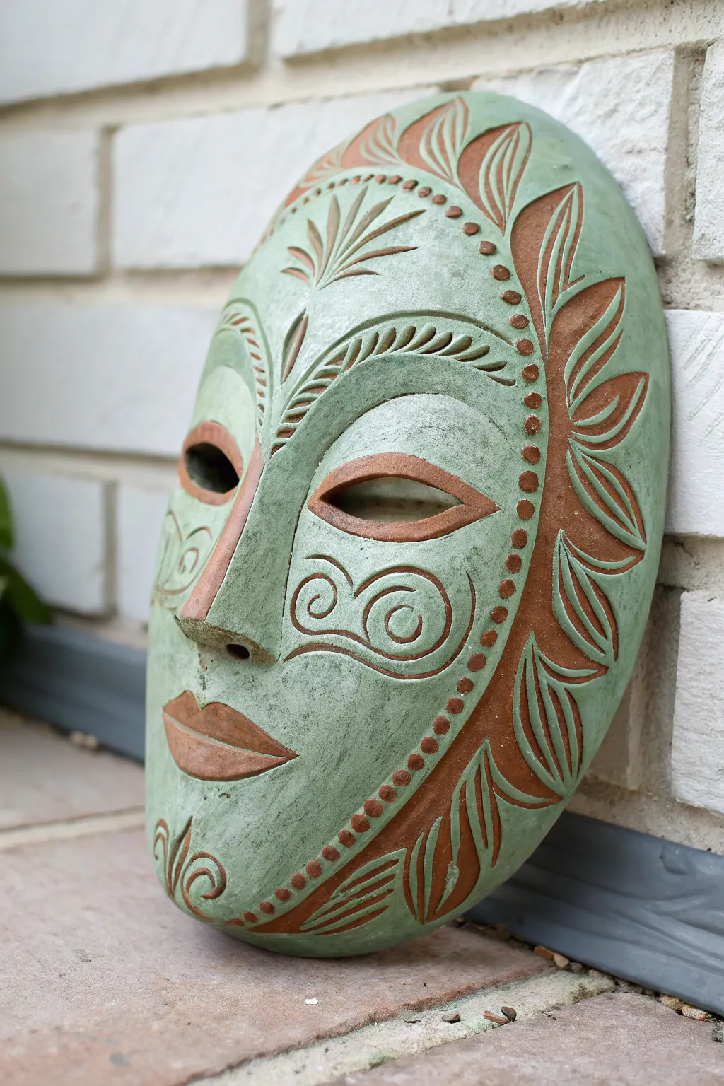 Sage slip sgraffito mask with bold carved lines revealing warm terracotta for striking contrast