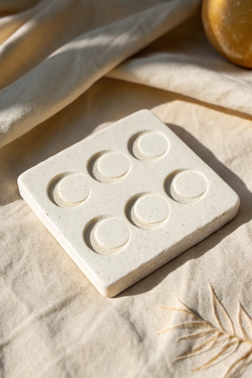 Minimal clay tile with raised moon phases in soft monochrome, serene and handmade.