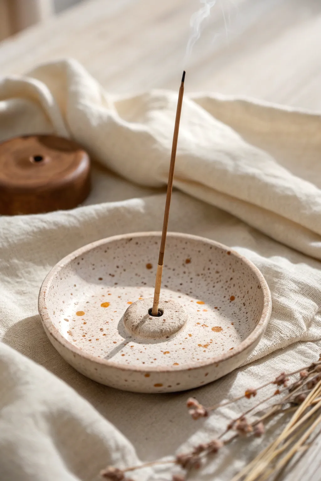 Minimal speckled clay incense dish with a centered hole, styled on soft neutral linen.