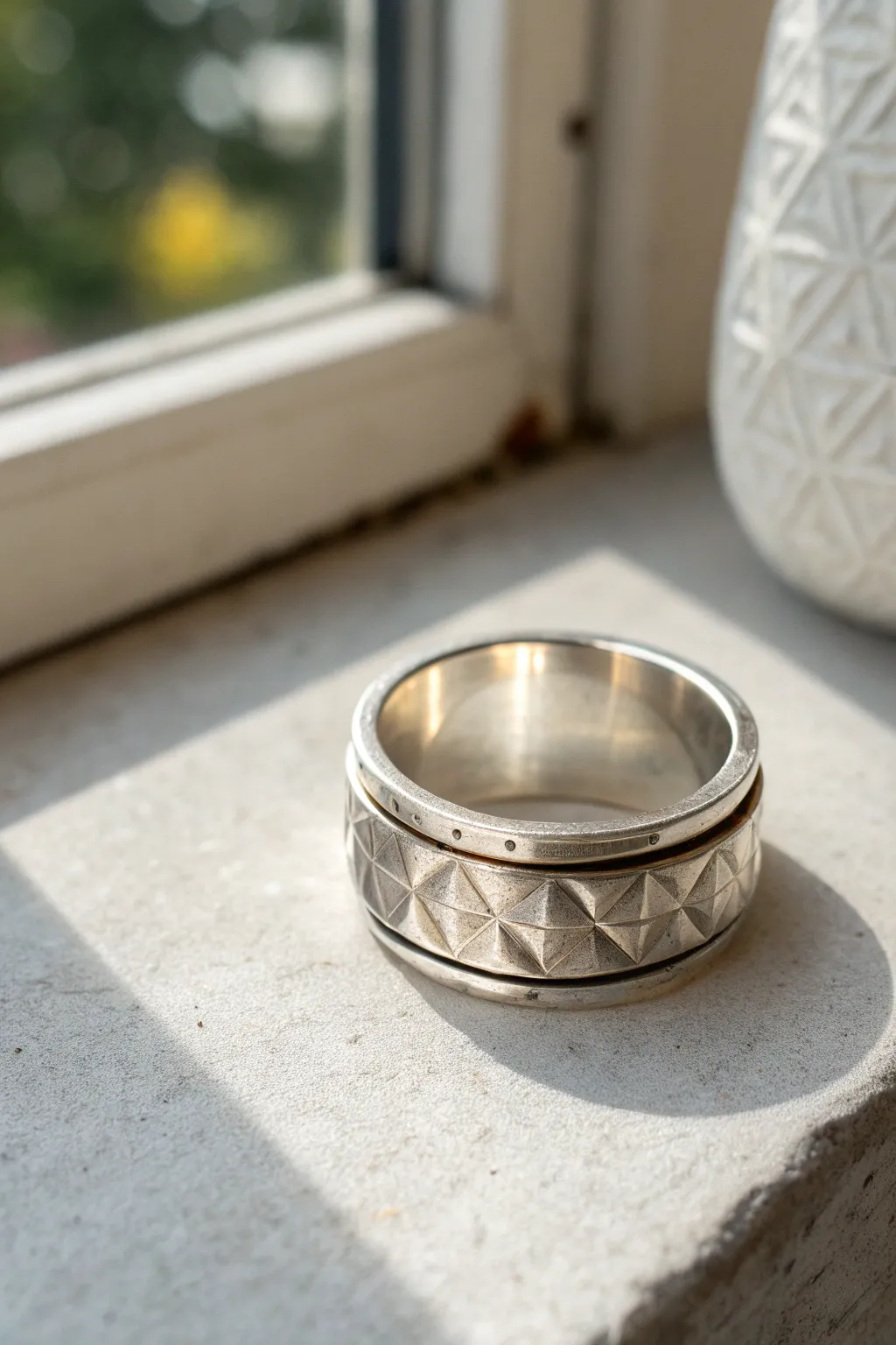 Minimal metal clay spinner ring with stamped texture, captured on concrete in soft Scandinavian light