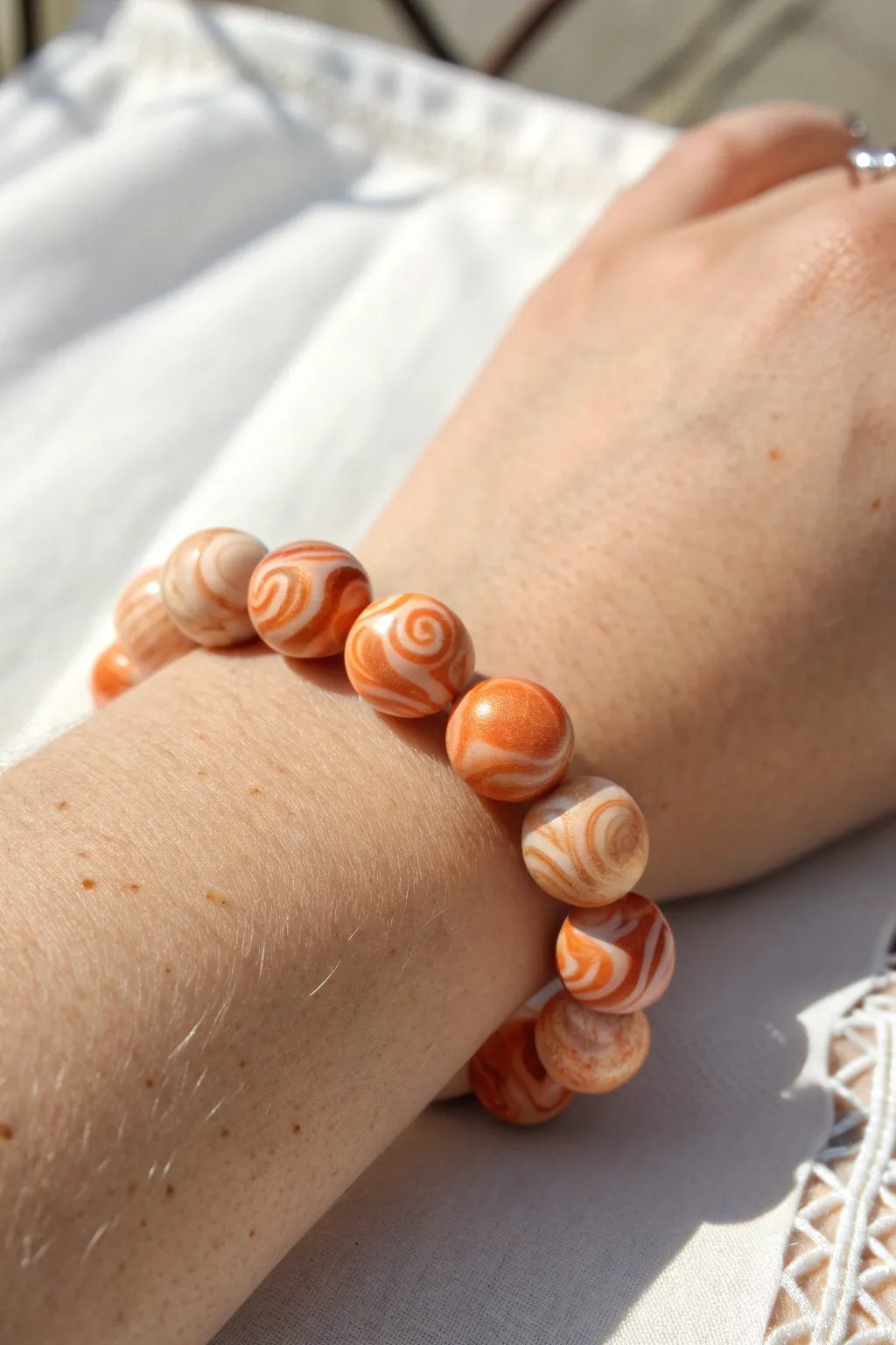 Marbled orange swirl clay bead bracelet glowing in soft sunlight, minimal and boho-chic.