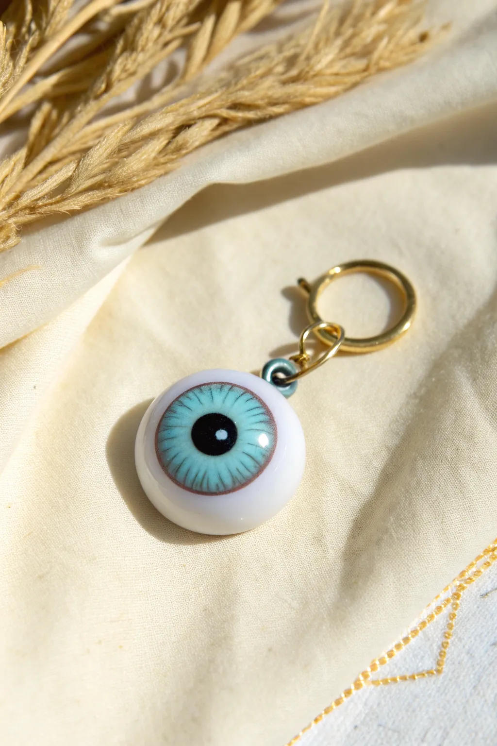 Glossy clay eyeball charm with a tiny loop, minimal backdrop and trippy vibes in crisp focus.