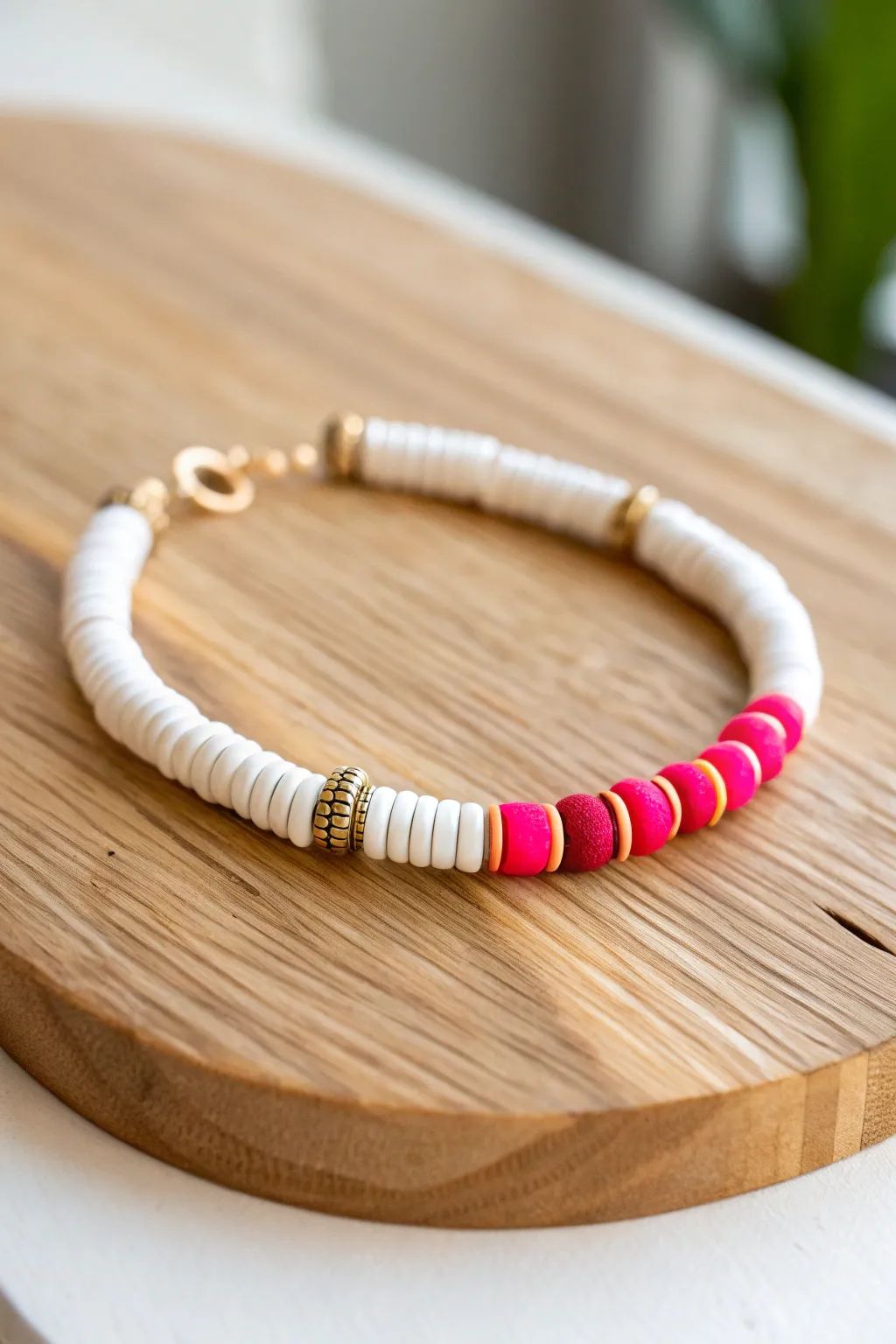 Mostly white heishi bracelet with bold red and hot pink pops and tiny gold spacers on warm wood.