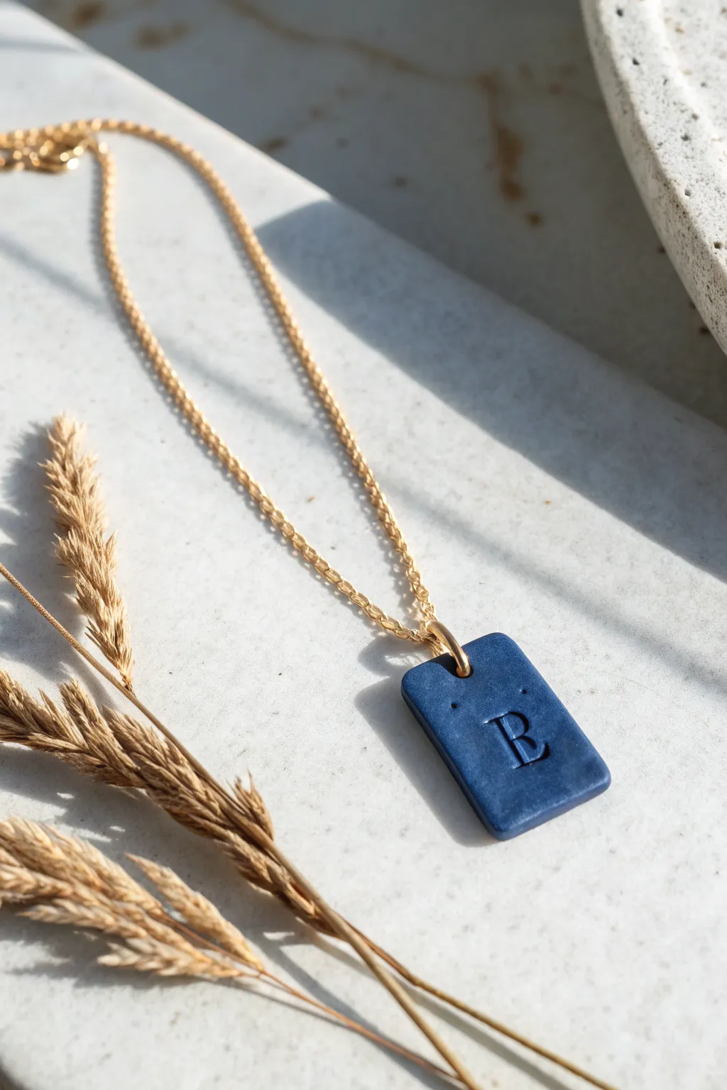 Air-dry clay initial tag necklace in bold cobalt, matte finish, minimalist flat lay inspiration.