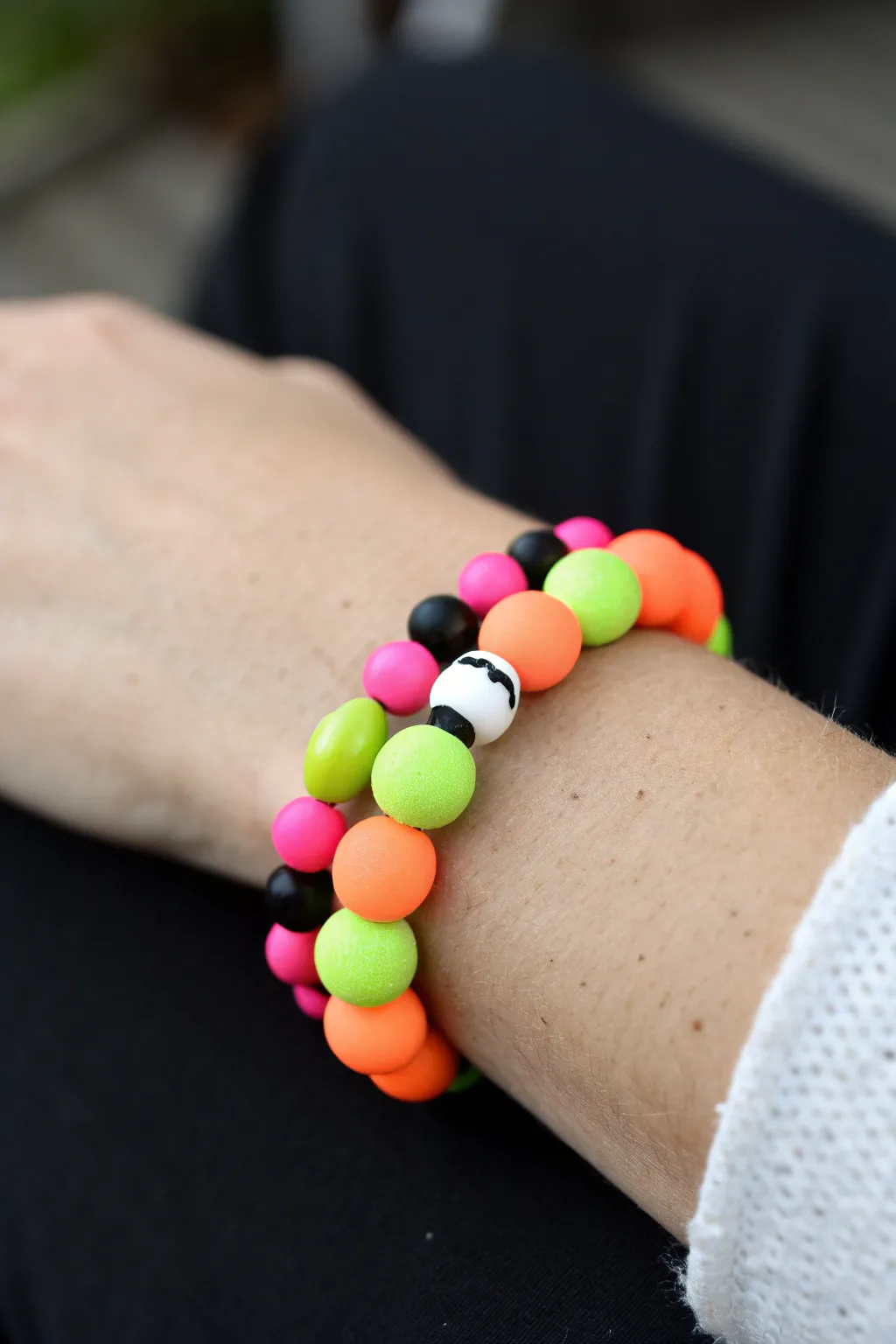 Neon glow birthday clay bead bracelet in hot pink, lime, and orange against a dark backdrop
