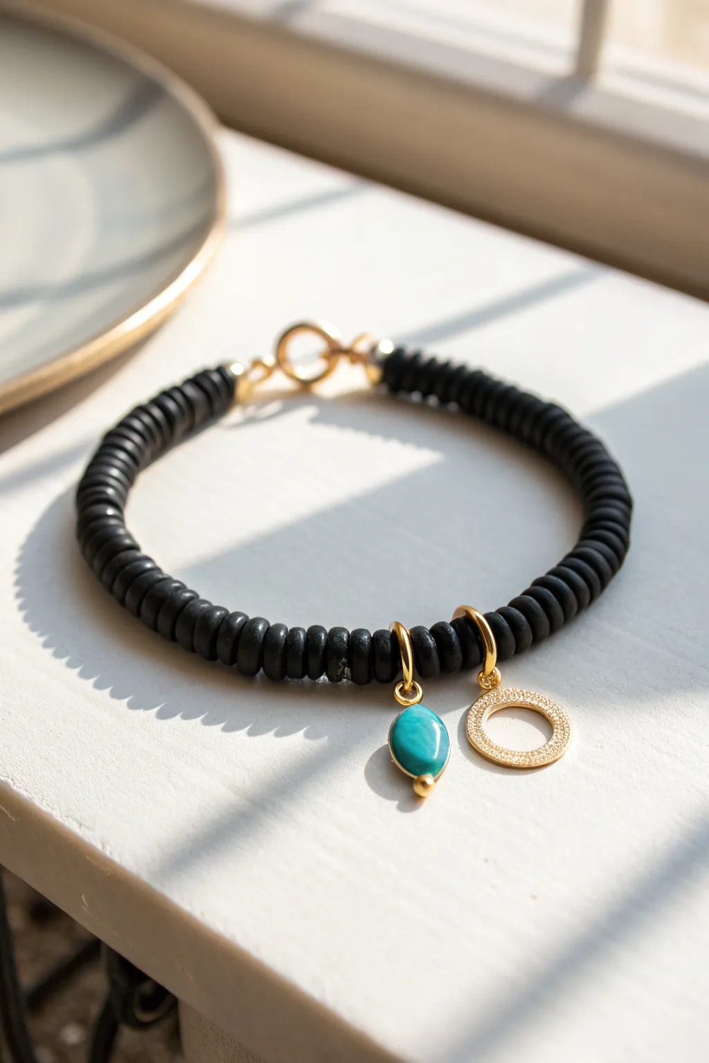 Minimal black heishi bead bracelet with delicate gold dangles, bold contrast on bright background
