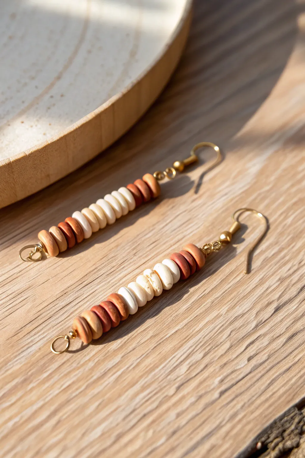 Marbled terracotta and cream heishi clay bead dangle earring on warm oak, minimalist boho.