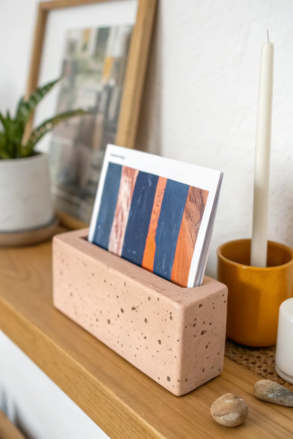 Minimal clay postcard slot holder in blush glaze, styled with candle and tiny plant on a shelf.