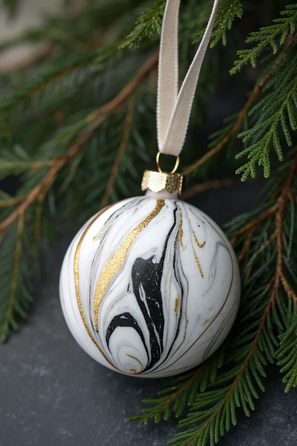 Striking faux marble clay bauble in black, white, and gold against deep evergreen greenery.