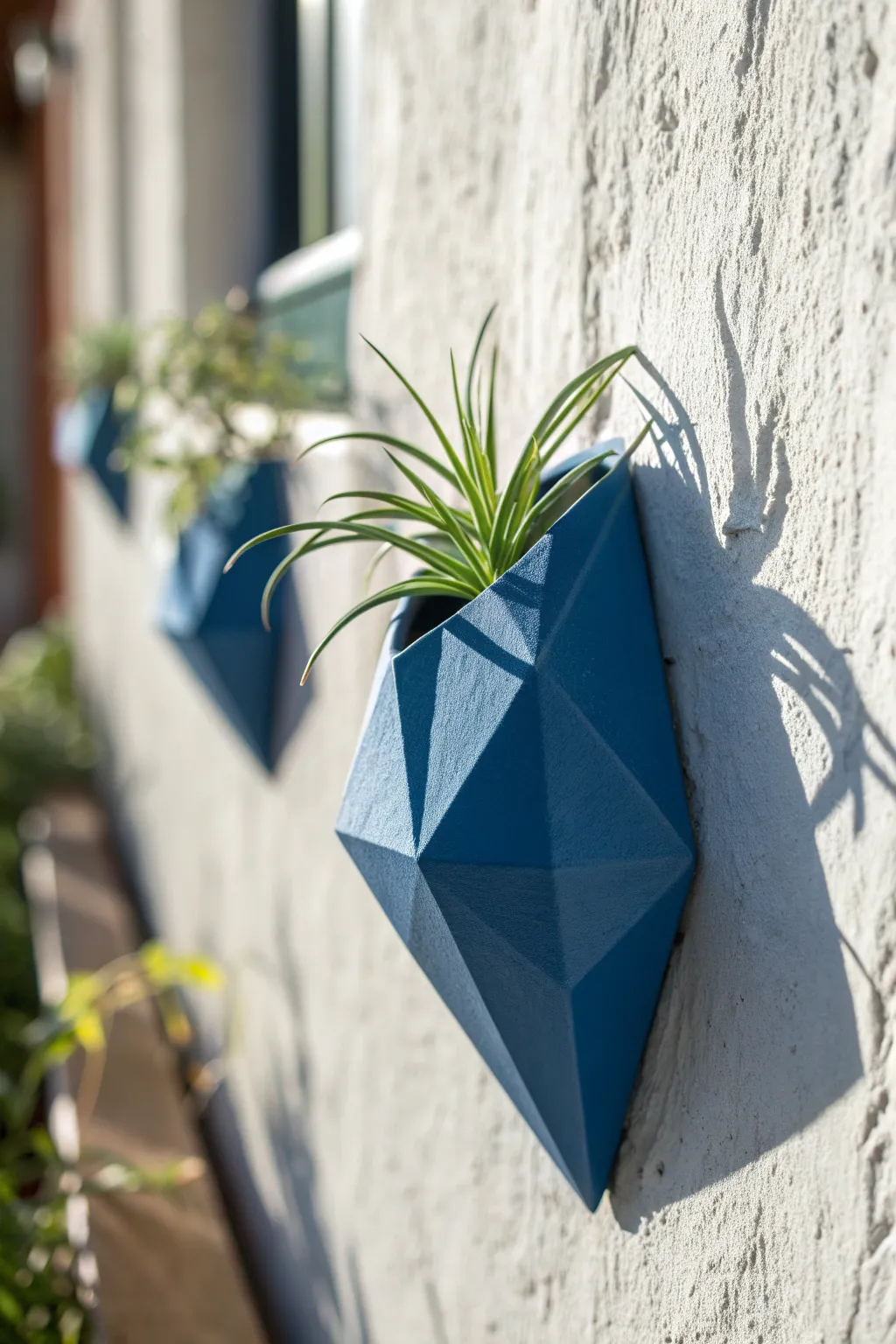 A bold faceted wall pocket in cobalt blue, finished cleanly and styled with a tiny air plant.