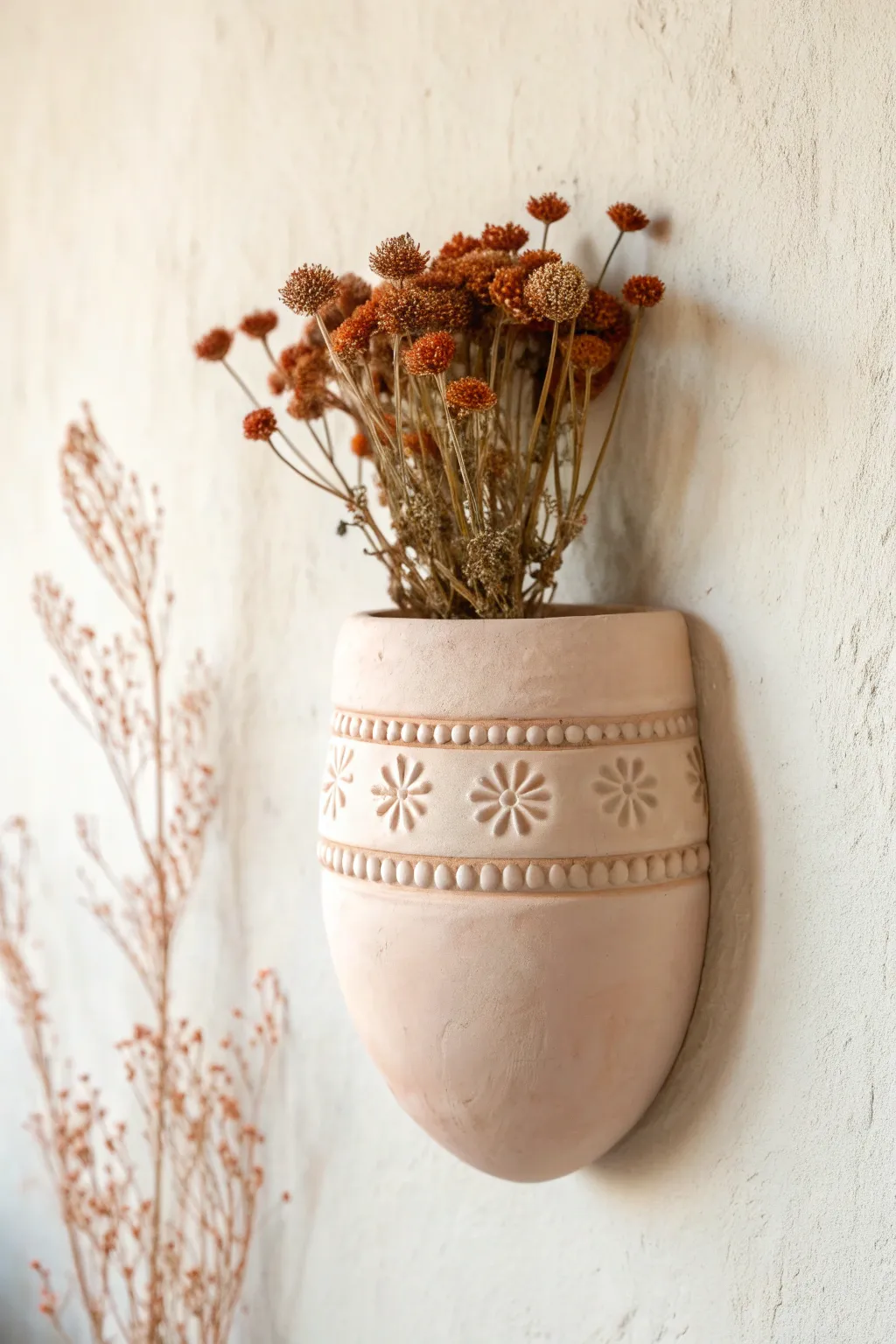Soft blush clay wall pocket with raised floral appliqué, styled with bold dried blooms