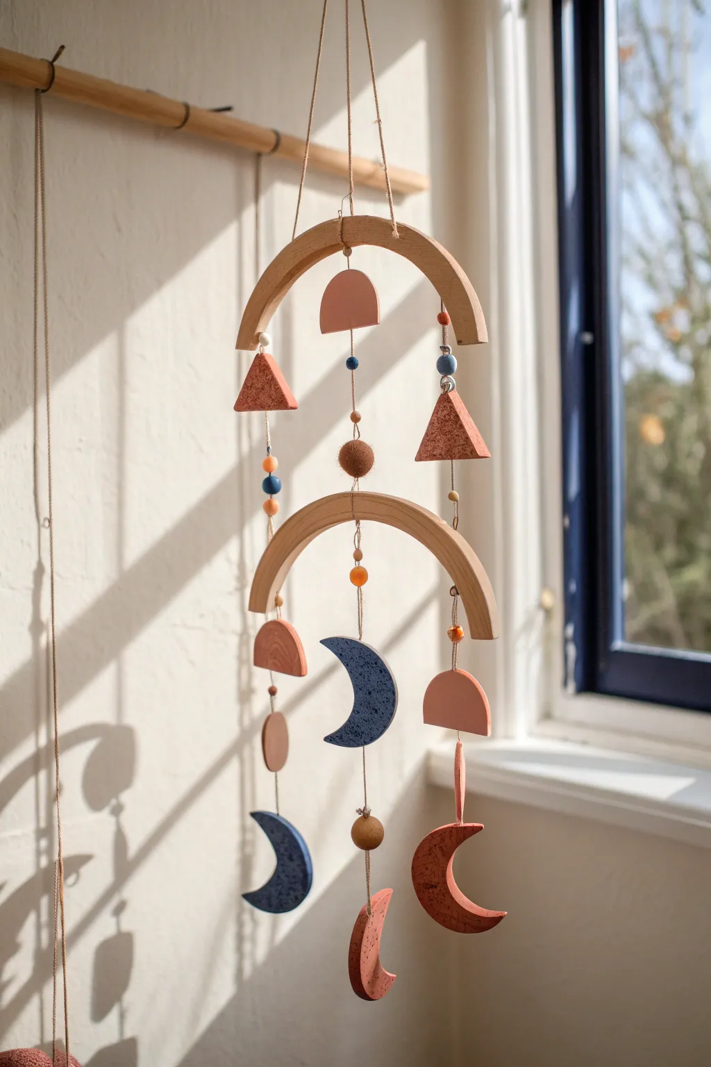 Simple geometric clay mobile in warm terracotta and blush, glowing in soft Scandinavian light.