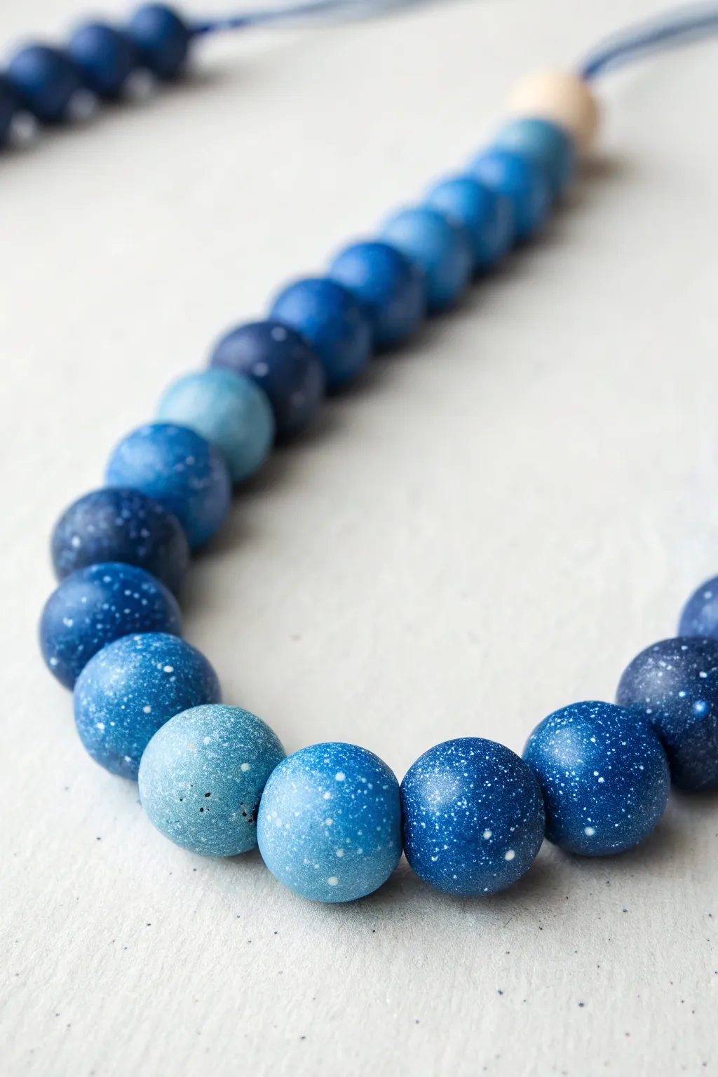 Ombre blue galaxy beads with starry speckles, curved on a clean backdrop for dreamy minimal style