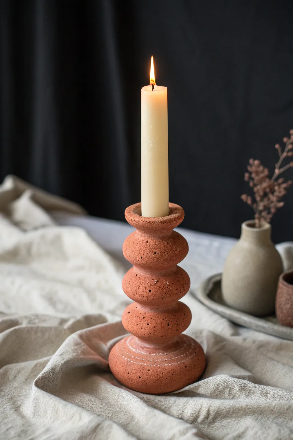 Handbuilt sculptural candle holder in bold terracotta, minimal styling, warm taper candle glow.