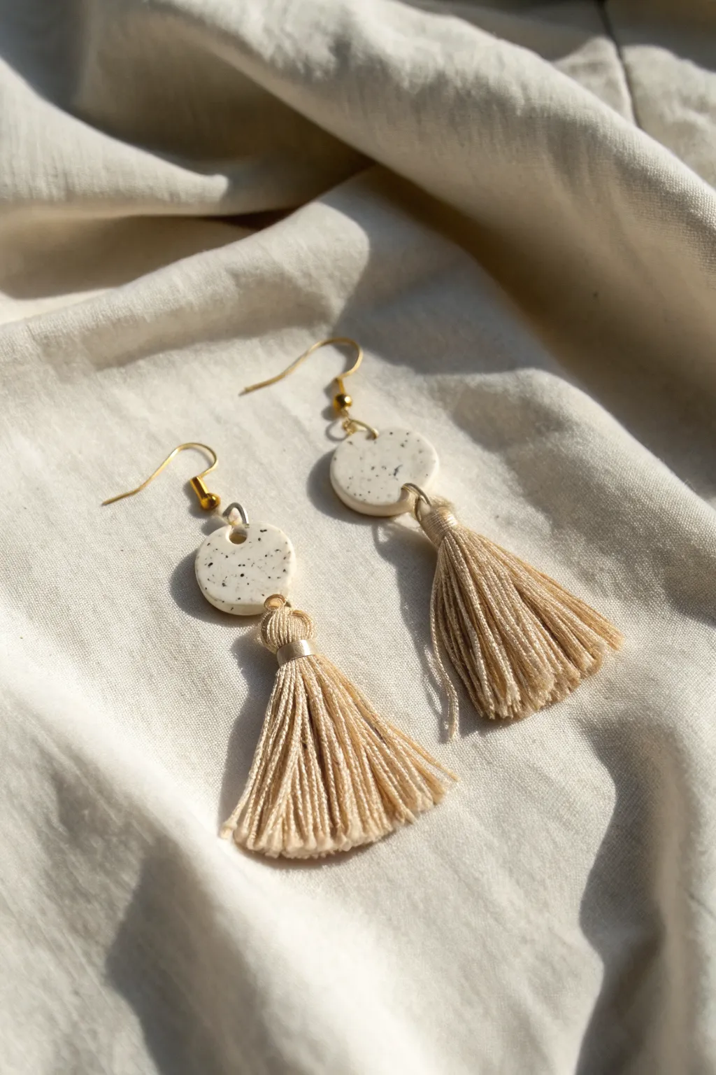Minimal boho tassel drop earrings with matte air-dry clay beads, styled on natural linen
