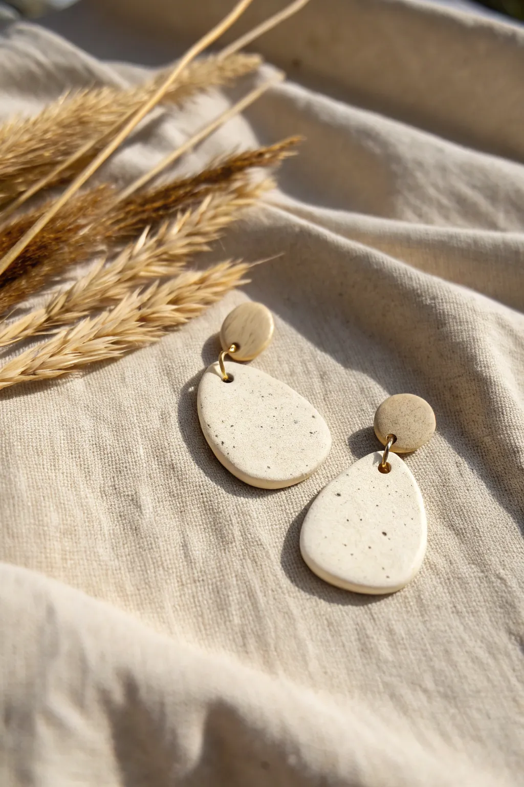 Chalky rustic air-dry clay earrings in soft sand tones, styled on linen for a cozy minimal look