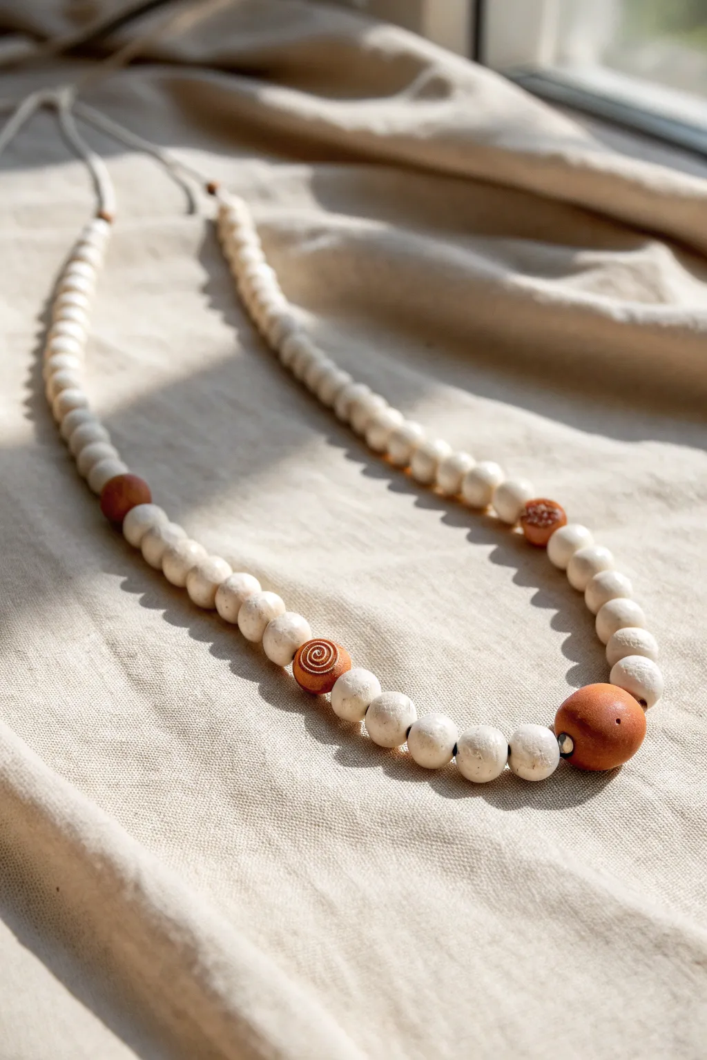 Minimal clay bead necklace with a stamped initial bead, softly styled on linen for a sweet mom gift