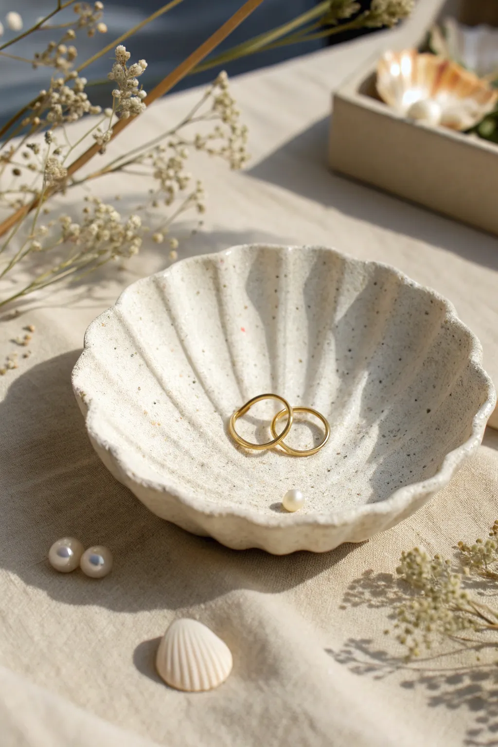 Shell-inspired clay dish with simple ridges, holding rings and studs on a soft sandy backdrop