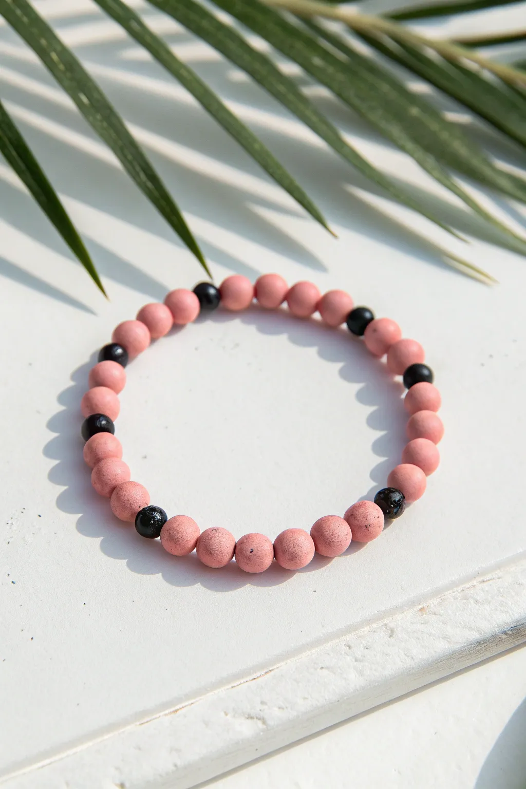 Pink clay bead bracelet with sleek black accents, minimalist contrast for modern boho style.