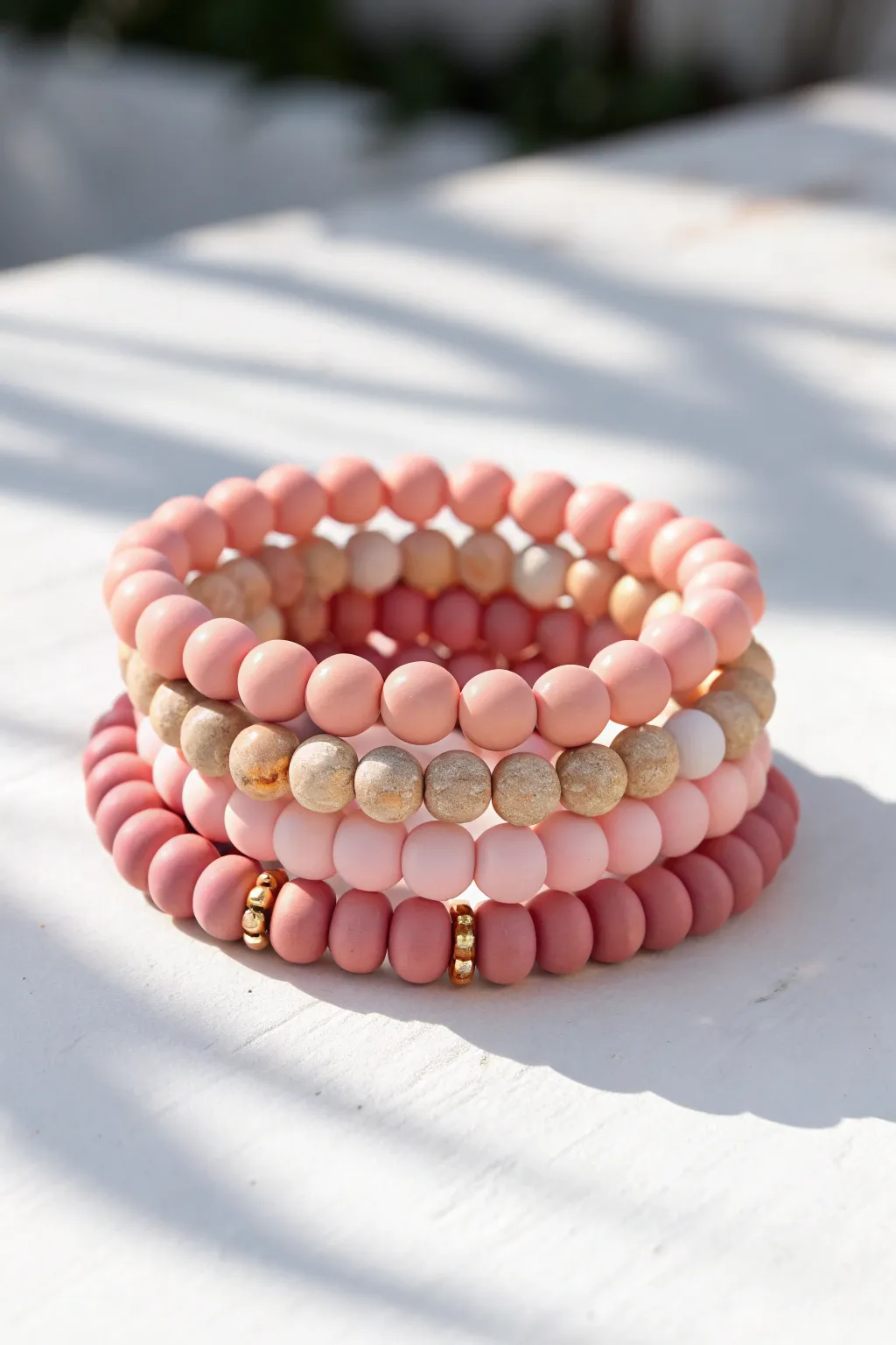 Monochrome pink clay bead bracelet stack with tiny gold spacers, crisp sunlight on white