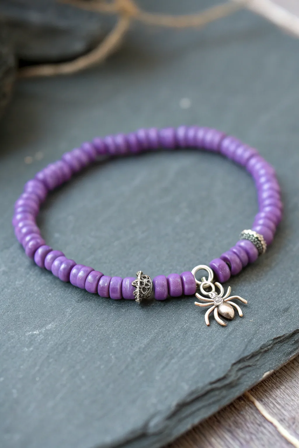 Purple heishi bracelet with a tiny spider accent, moody minimal styling for subtle spooky charm.