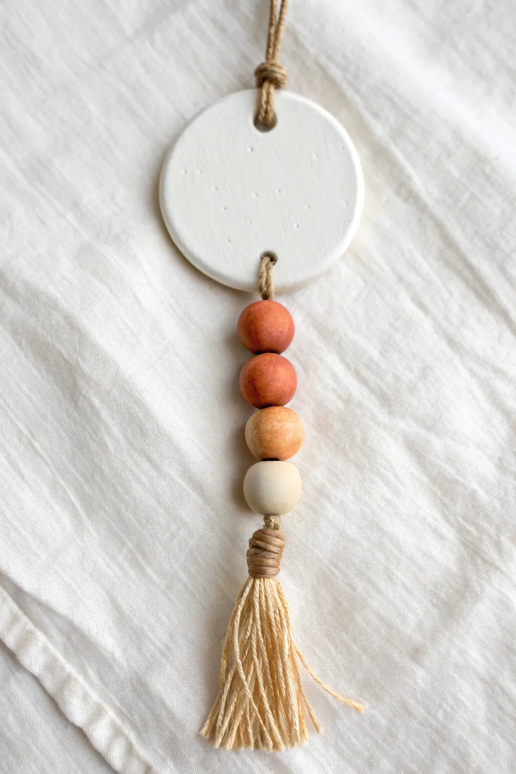 Minimal air-dry clay bead drop ornament with twine and a natural wooden bead, soft neutral tones.