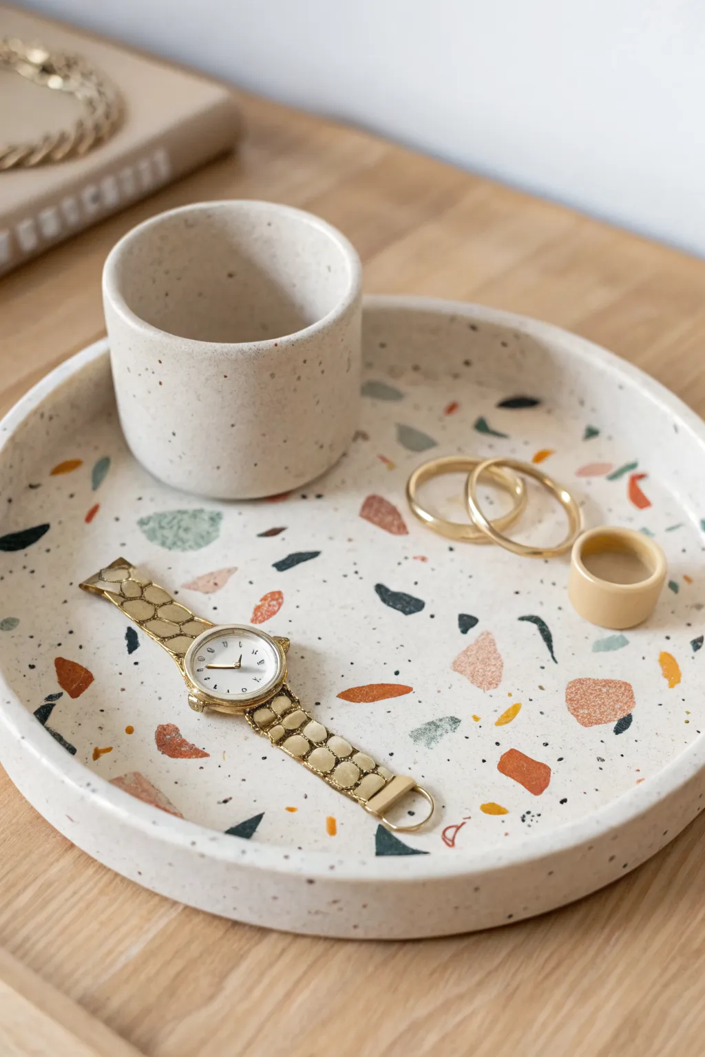 Minimal terrazzo air dry clay catchall tray styled with rings, a watch, and a soft candle glow